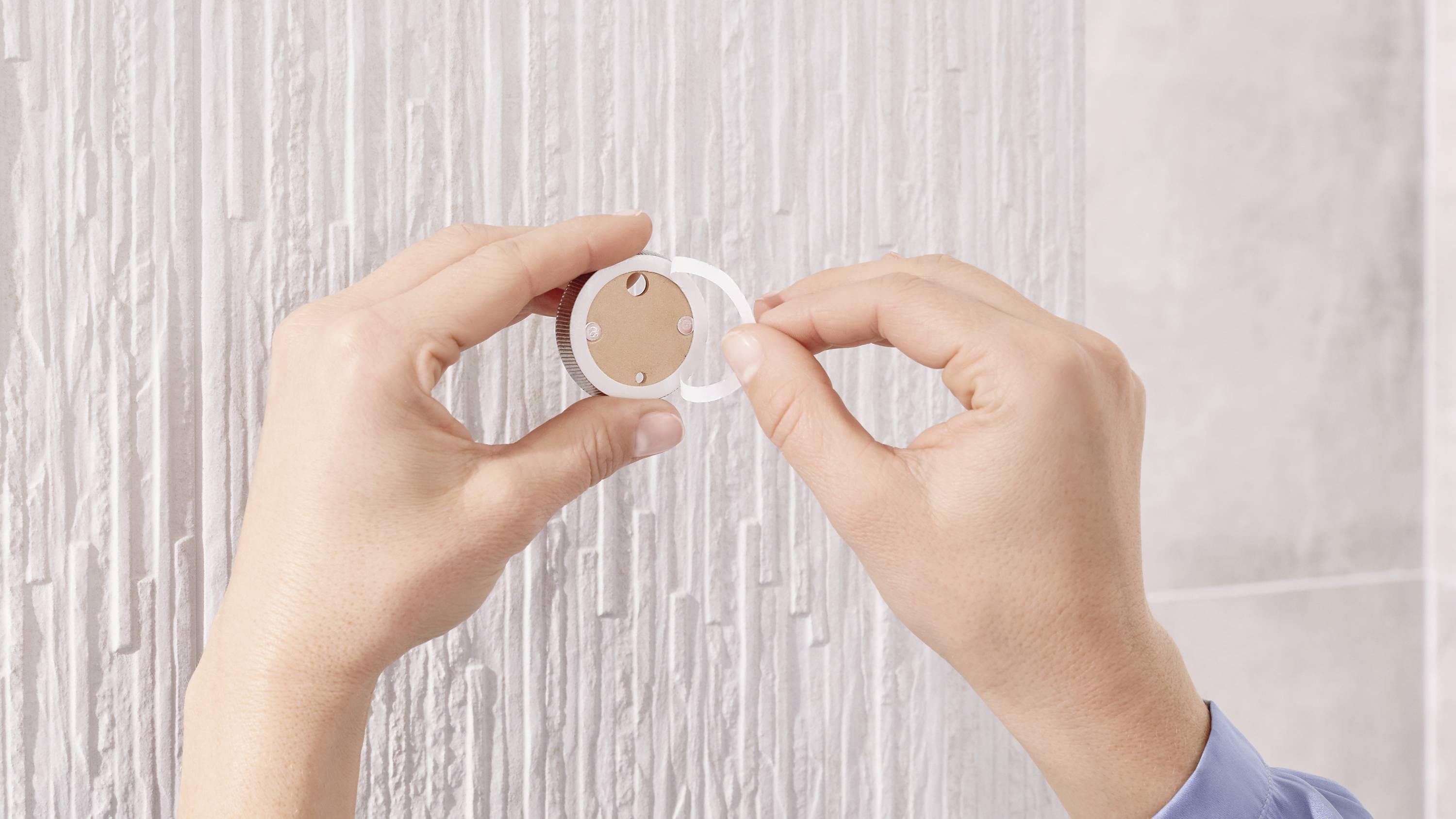 Une personne fixe une horloge murale ronde blanche sur un mur blanc texturé.