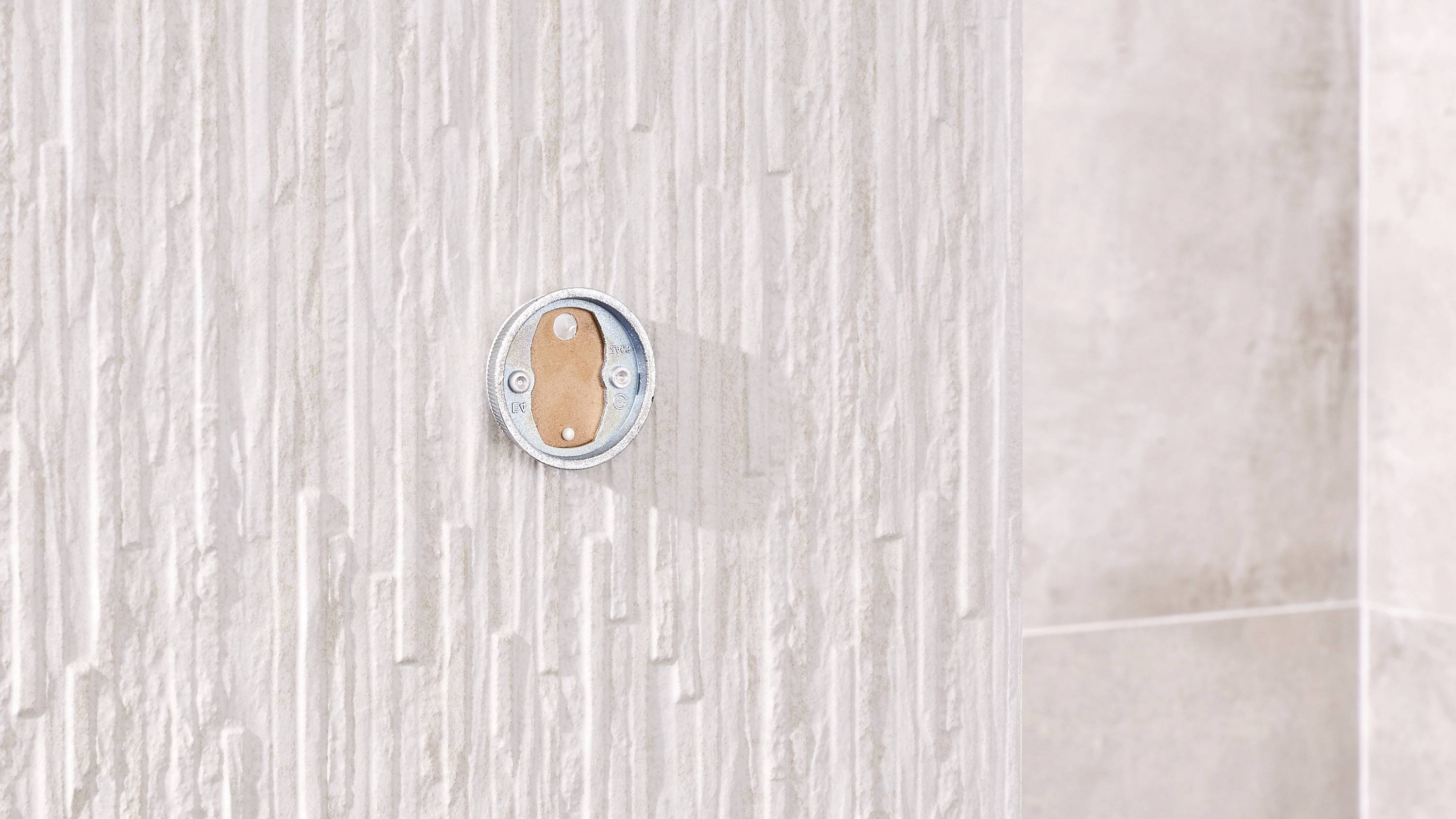 Mur blanc et structuré avec un objet métallique rond en son centre.