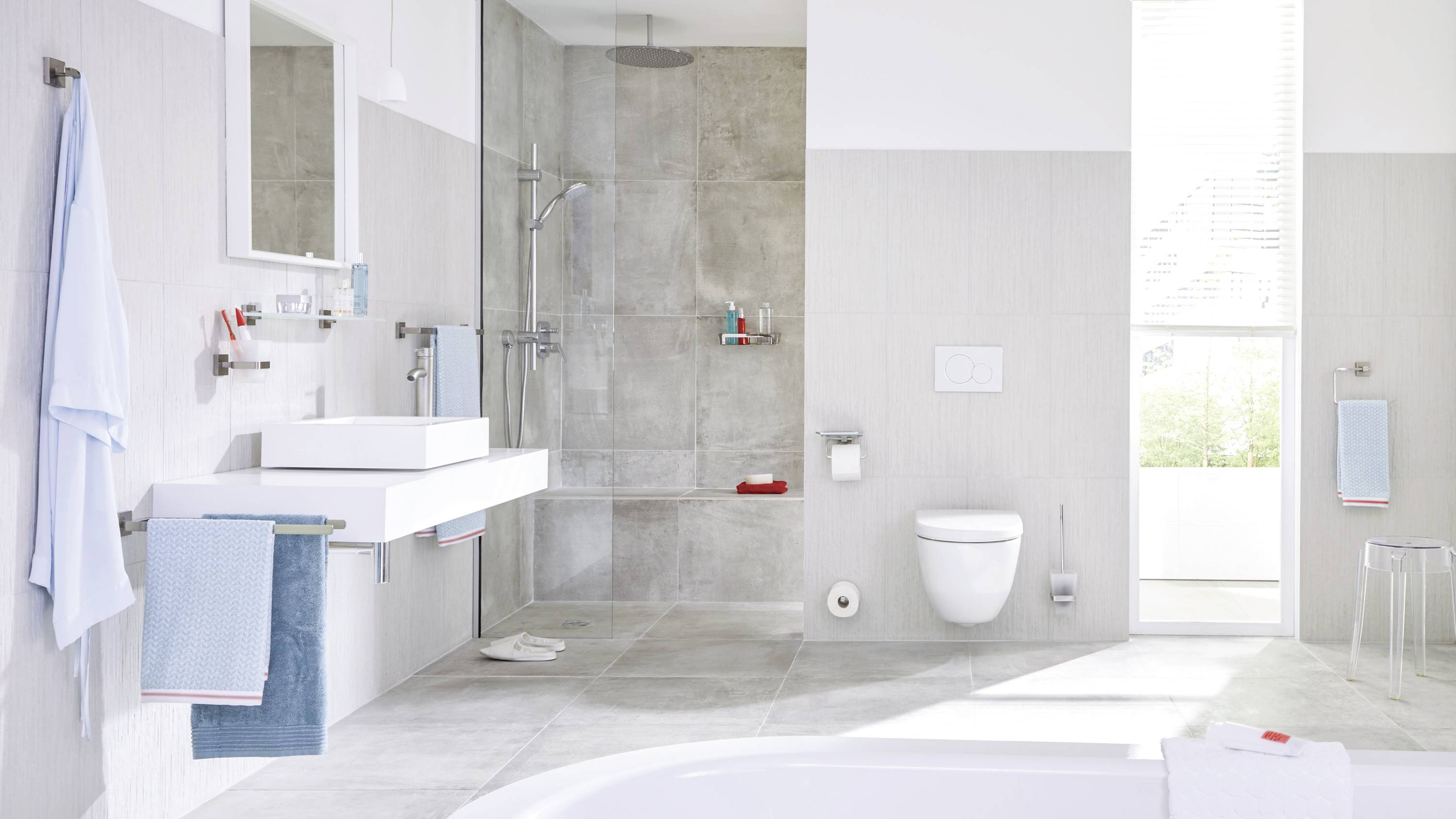 Salle de bain moderne avec des carreaux gris, douche, lavabo, toilettes et serviettes dans des tons bleus et blancs. Atmosphère lumineuse et épurée.