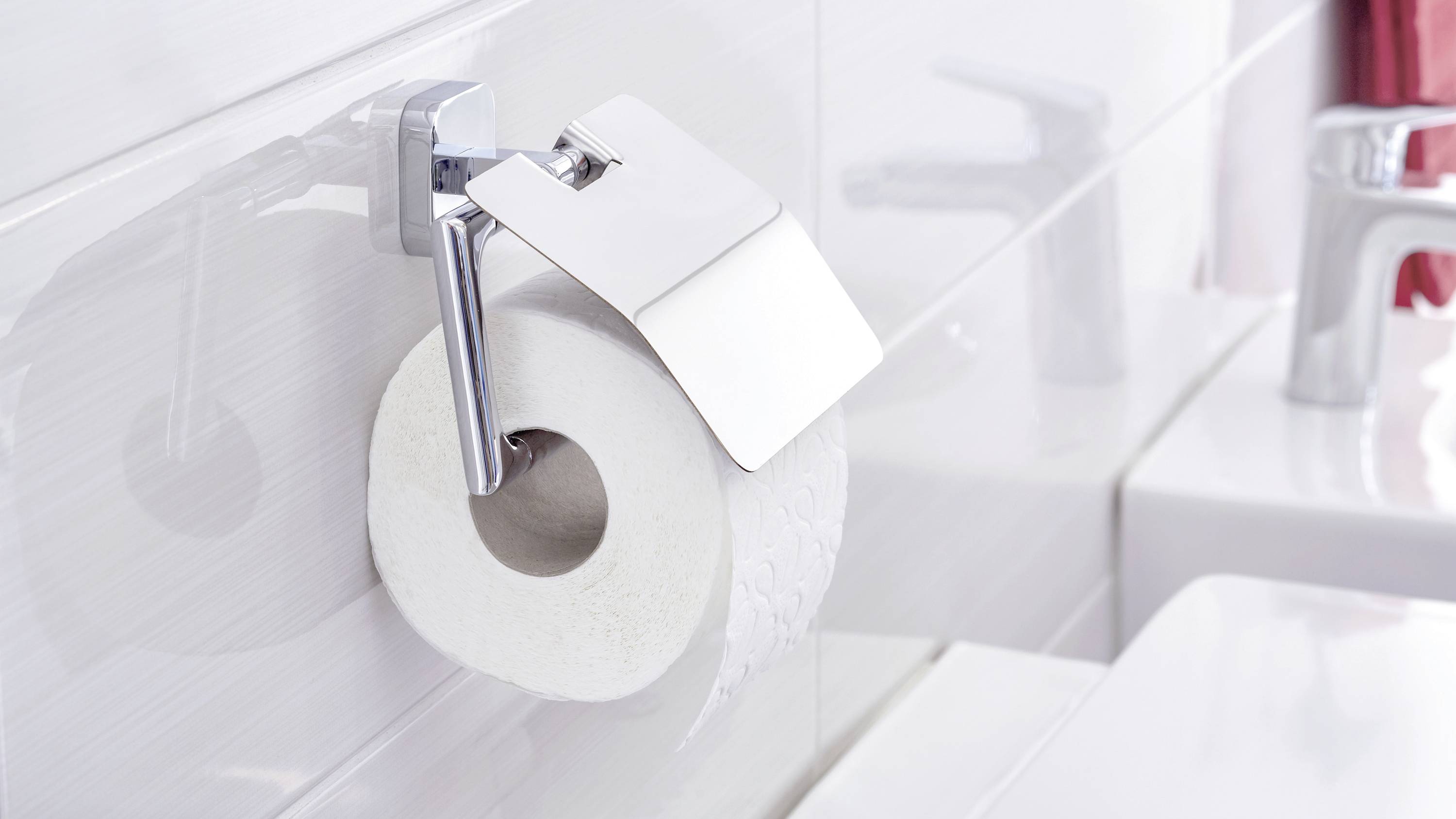 Une toilette avec un support de papier toilette blanc sur lequel est suspendu un rouleau de papier toilette ; à côté, un lavabo avec un robinet.