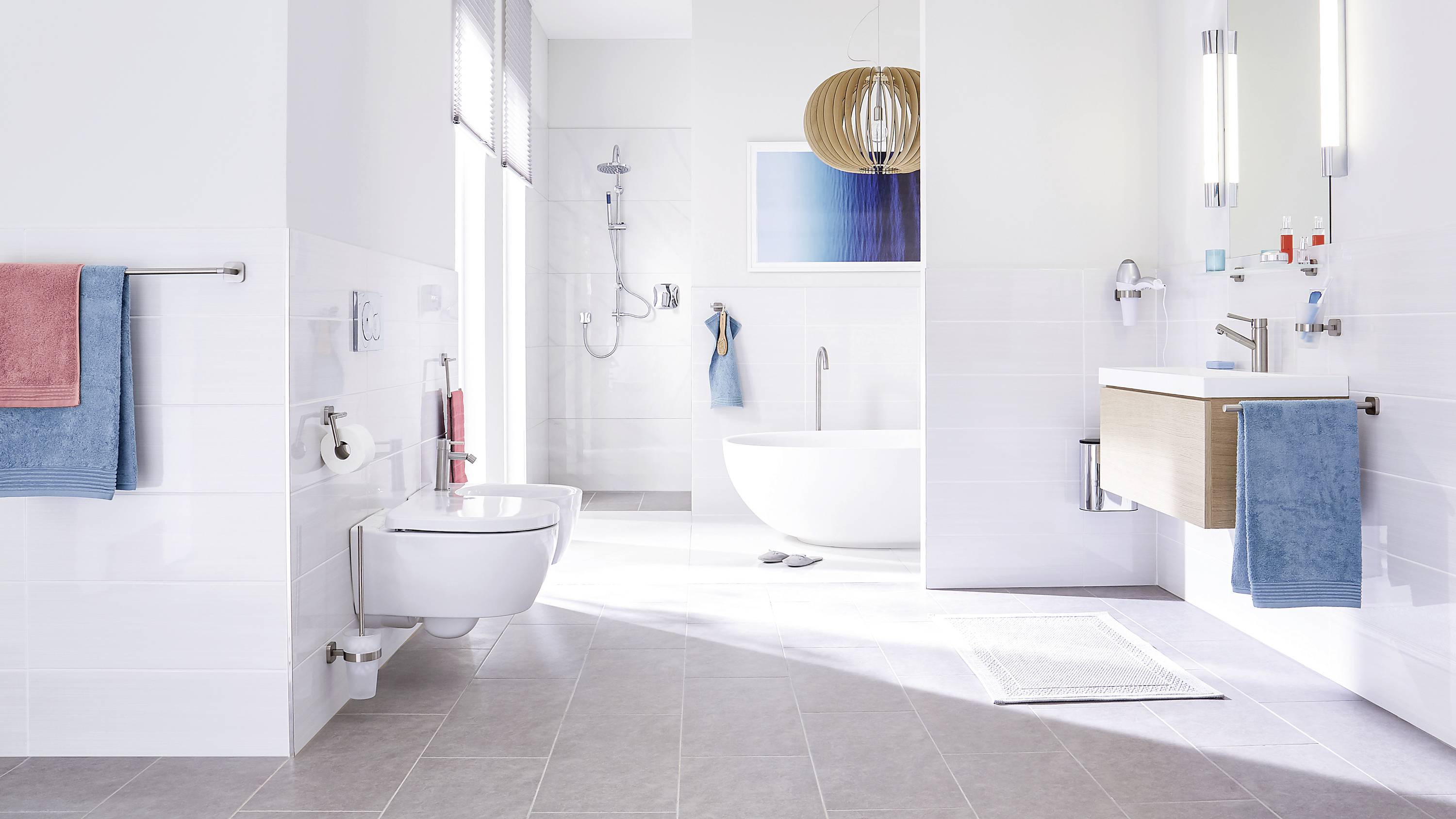 Salle de bain lumineuse et moderne avec baignoire îlot, espace douche, lavabo et toilettes. Des serviettes bleu et rouge apportent des touches de couleur.