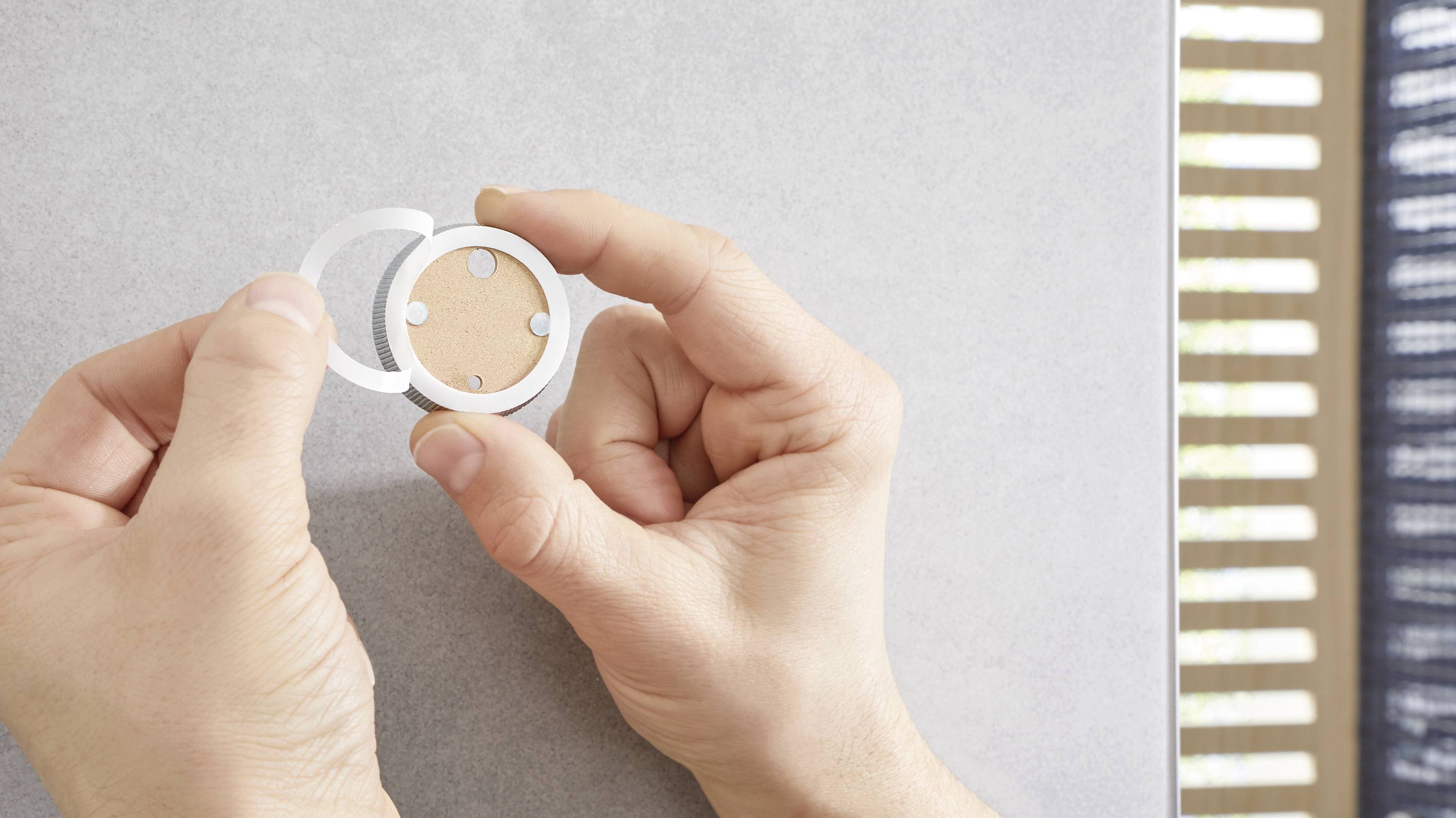 Deux mains tiennent un objet magnétique rond contre une surface grise.