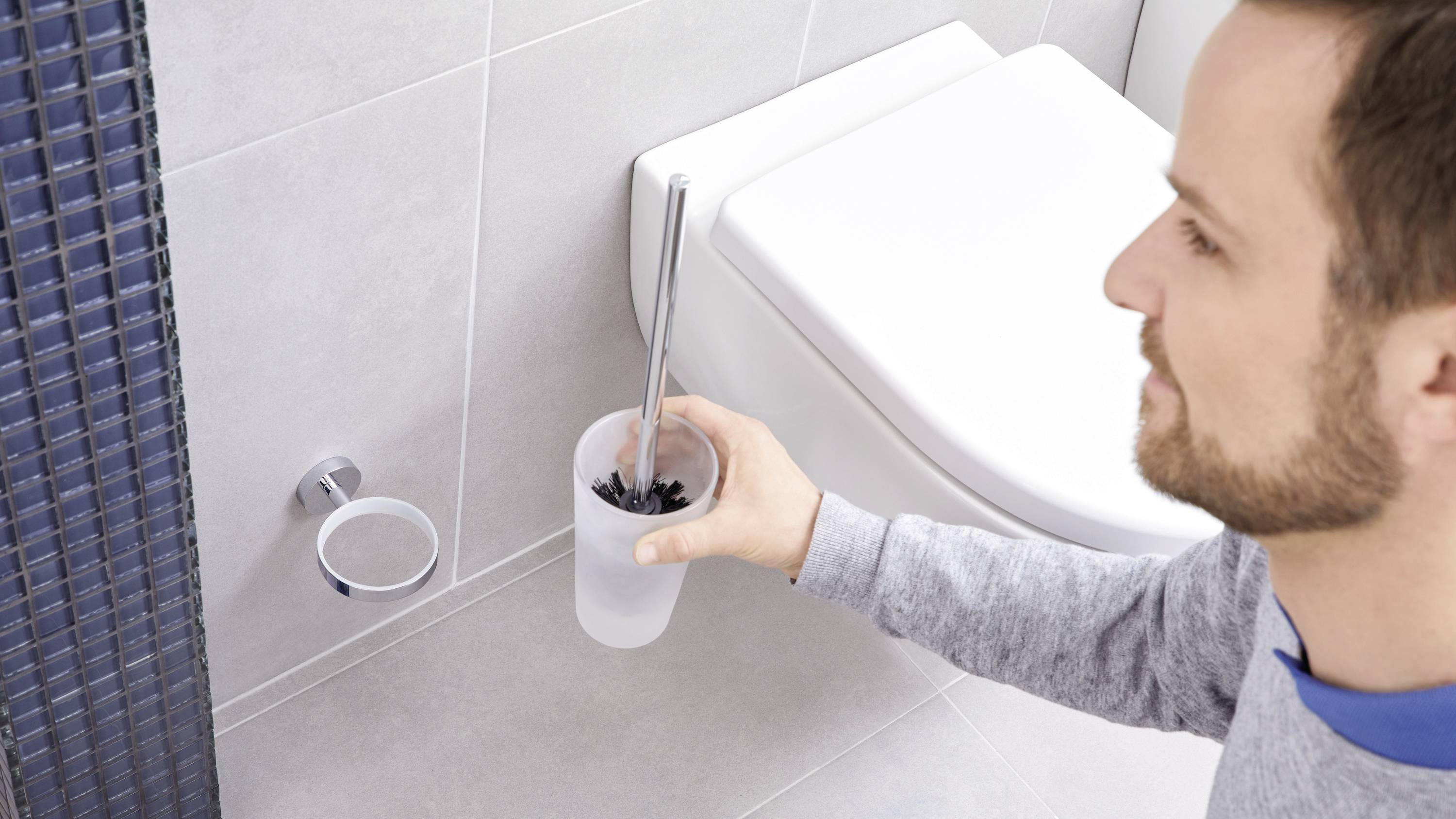 Une personne nettoie les toilettes avec une brosse de toilette. Un mur de salle de bain carrelé est visible en arrière-plan.