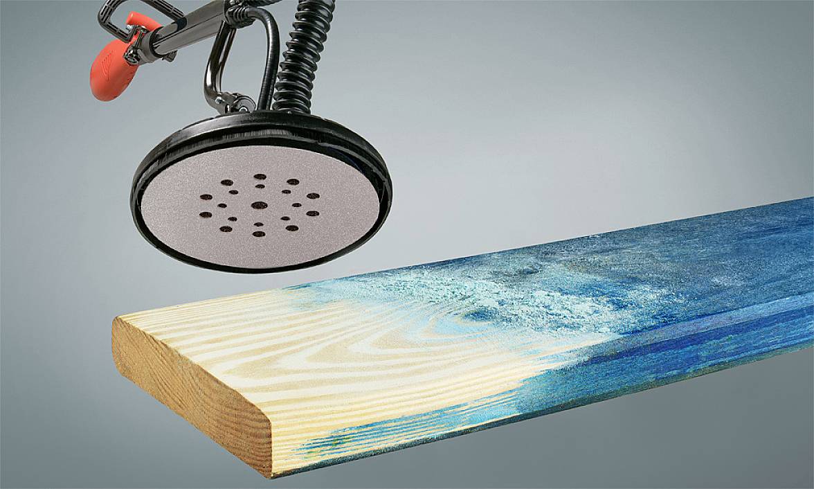 Une ponceuse enlève la peinture bleue d'un morceau de bois pour en révéler le grain original.