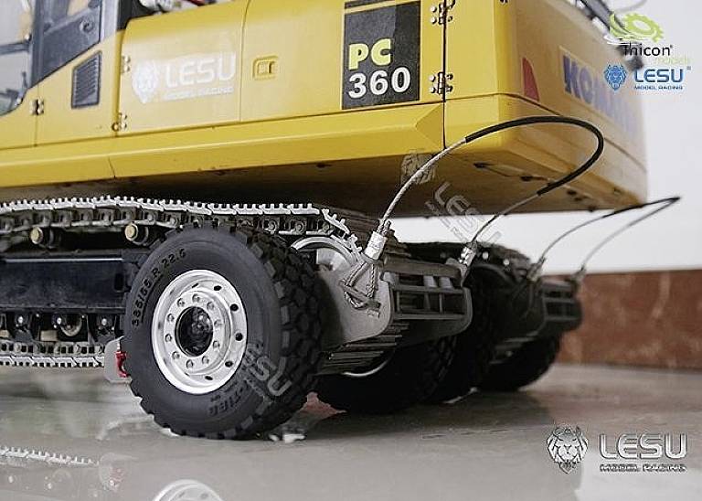 Pelleteuse jaune sur pneus et chenilles métalliques, gros plan sur les roues arrière et le mécanisme de chenilles, devant un mur de marbre.