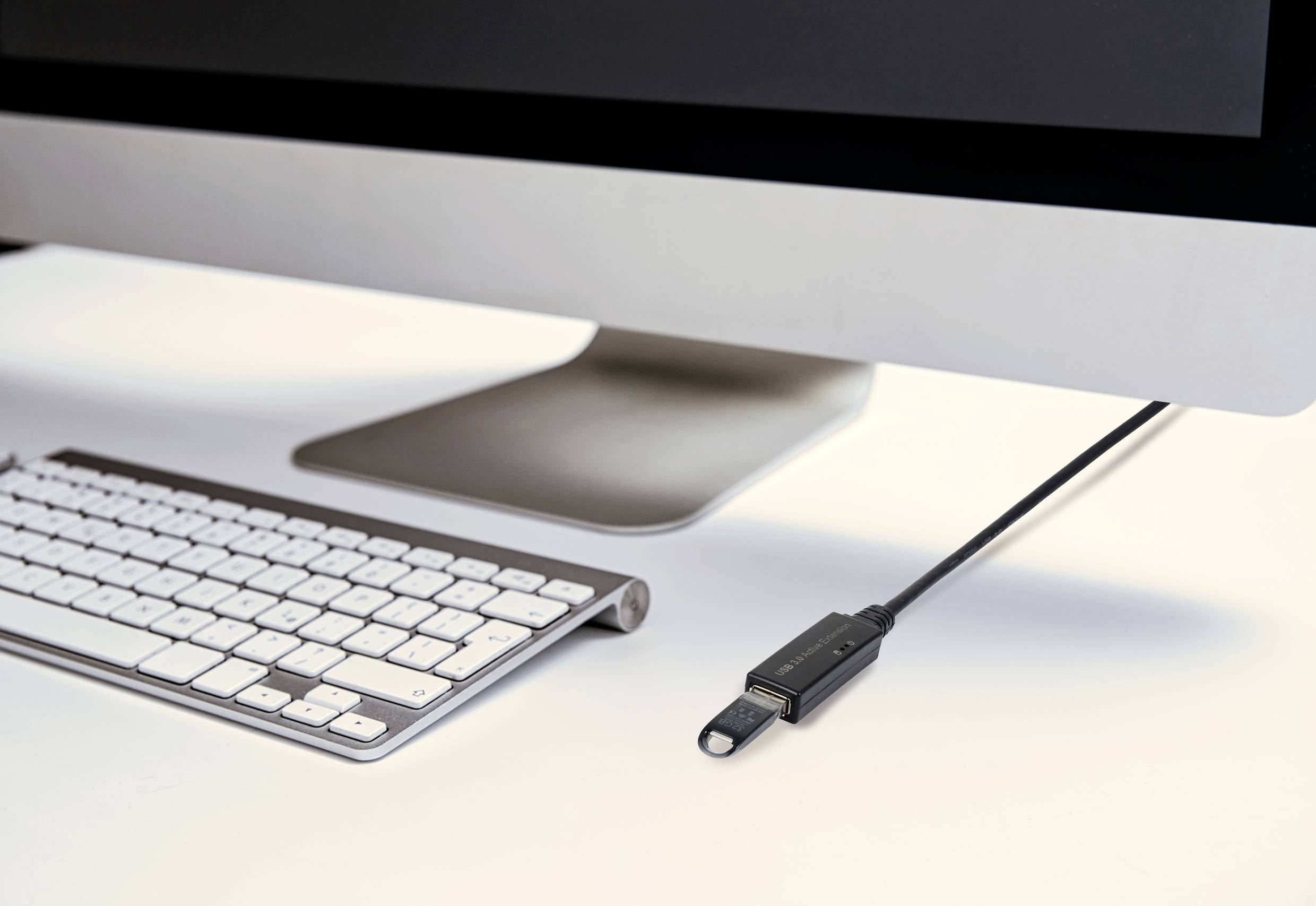 Un écran d'ordinateur sur un bureau, avec un clavier devant et une clé USB branchée sur le côté du moniteur.