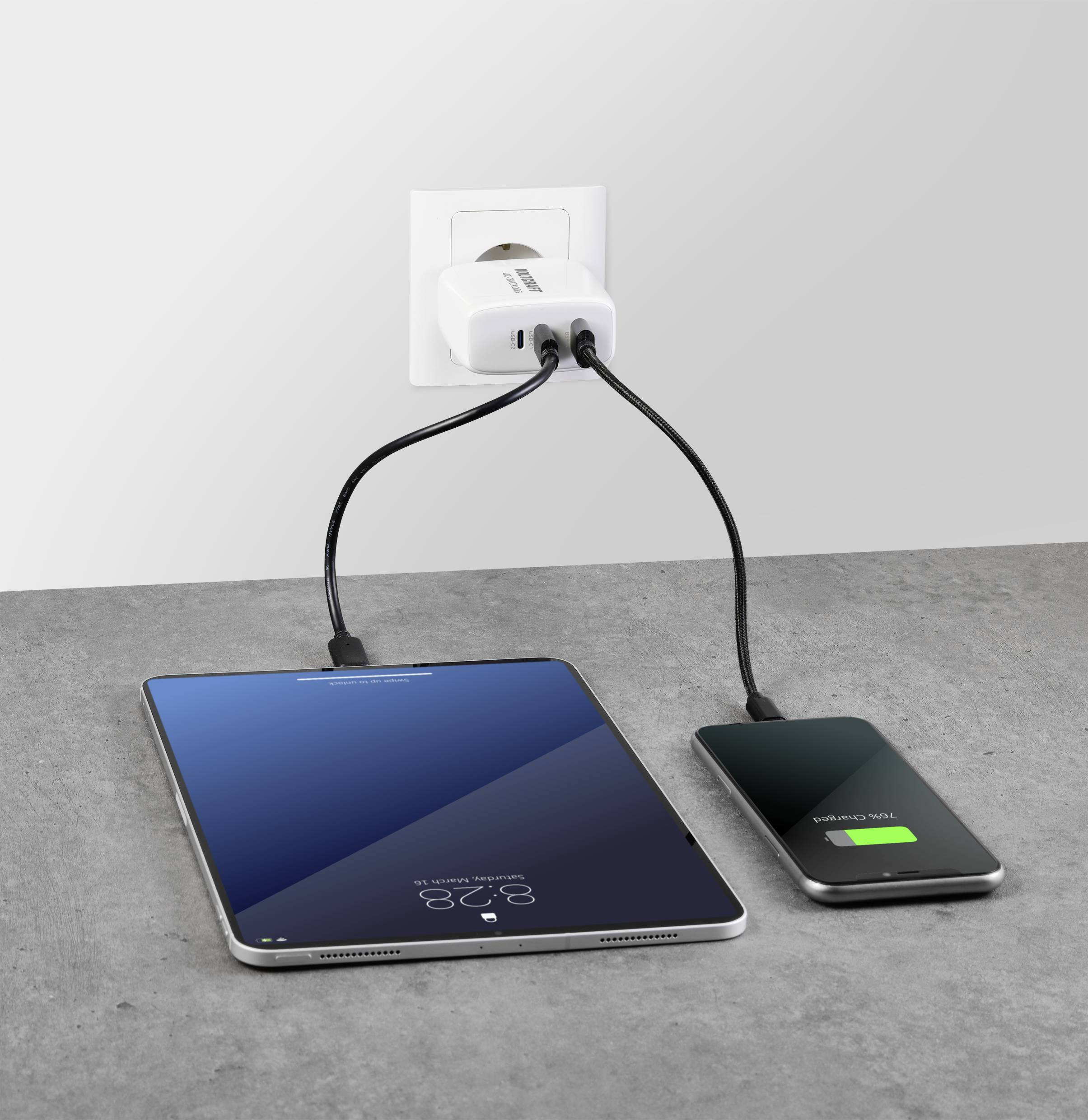 Une tablette et un smartphone sont en train de charger simultanément à une prise électrique. Le smartphone affiche une barre de chargement verte.