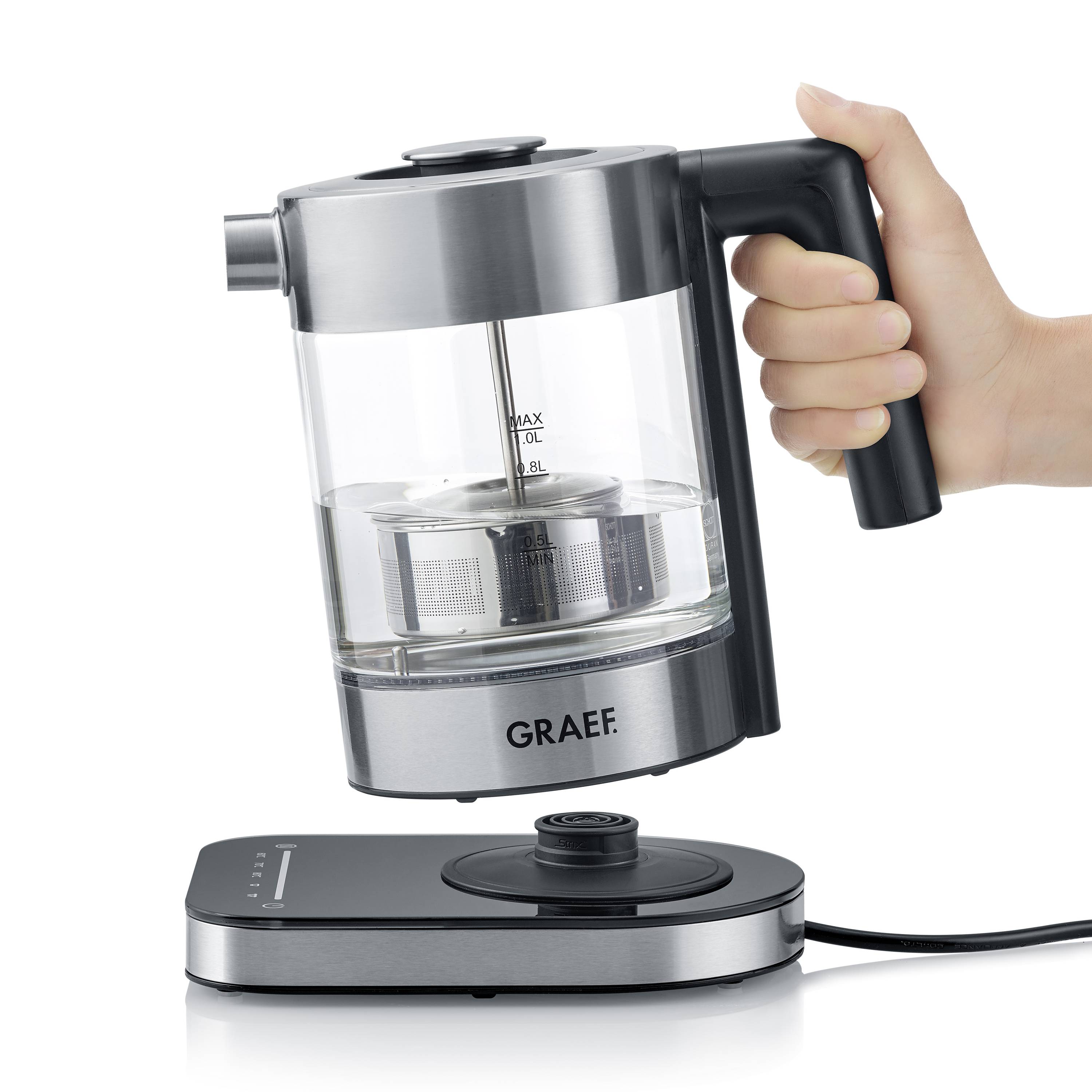 Une bouilloire électrique avec un récipient transparent reposant sur une base métallique. Une main tient la poignée.