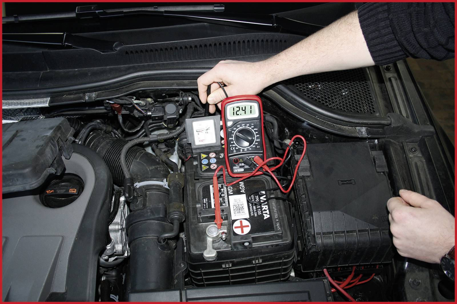 Une personne mesure la tension d'une batterie de voiture avec un multimètre. L'affichage indique '12,41'.