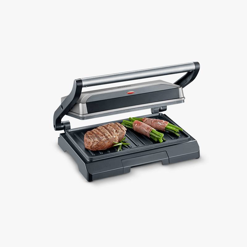 Un grill électrique à contact avec le couvercle ouvert fait griller deux steaks et des asperges vertes enroulées de lard.