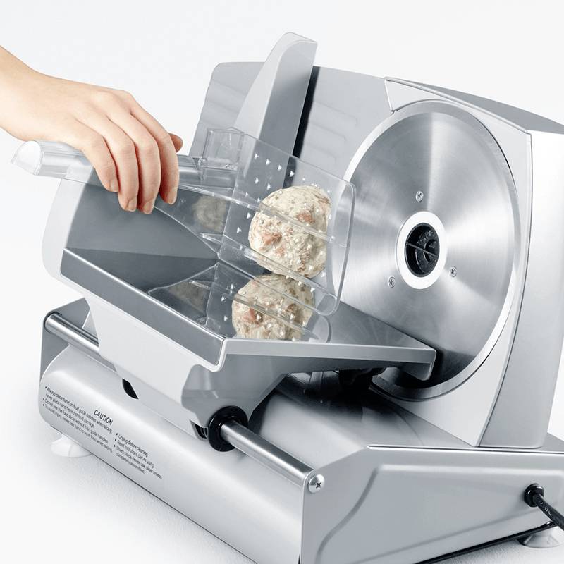 Une personne coupe une pâte en tranches à l'aide d'une machine électrique à trancher le pain. La pâte contient des noix ou des fruits.
