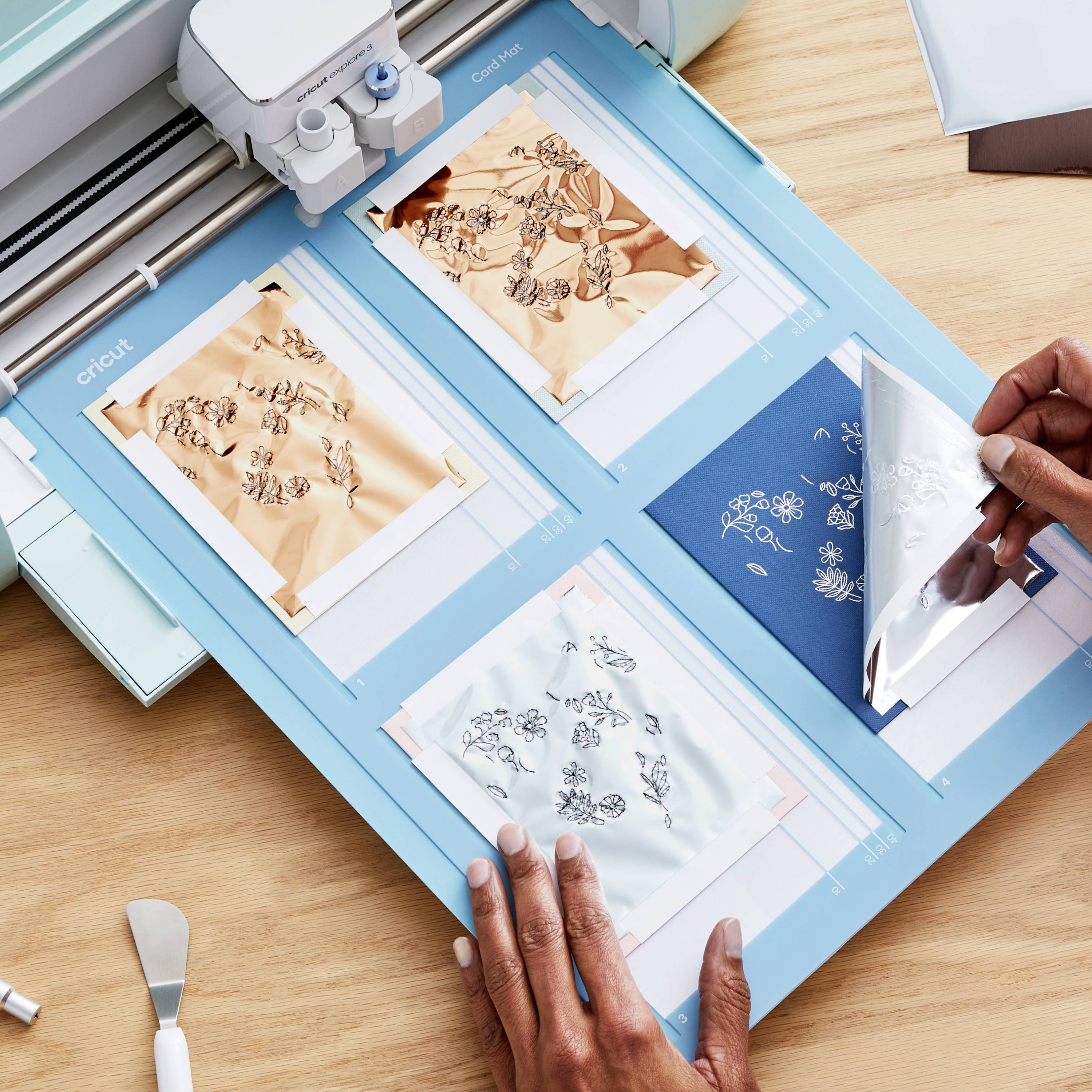 Une personne utilise un outil de découpe pour transférer avec précision des motifs floraux sur une feuille bleue.