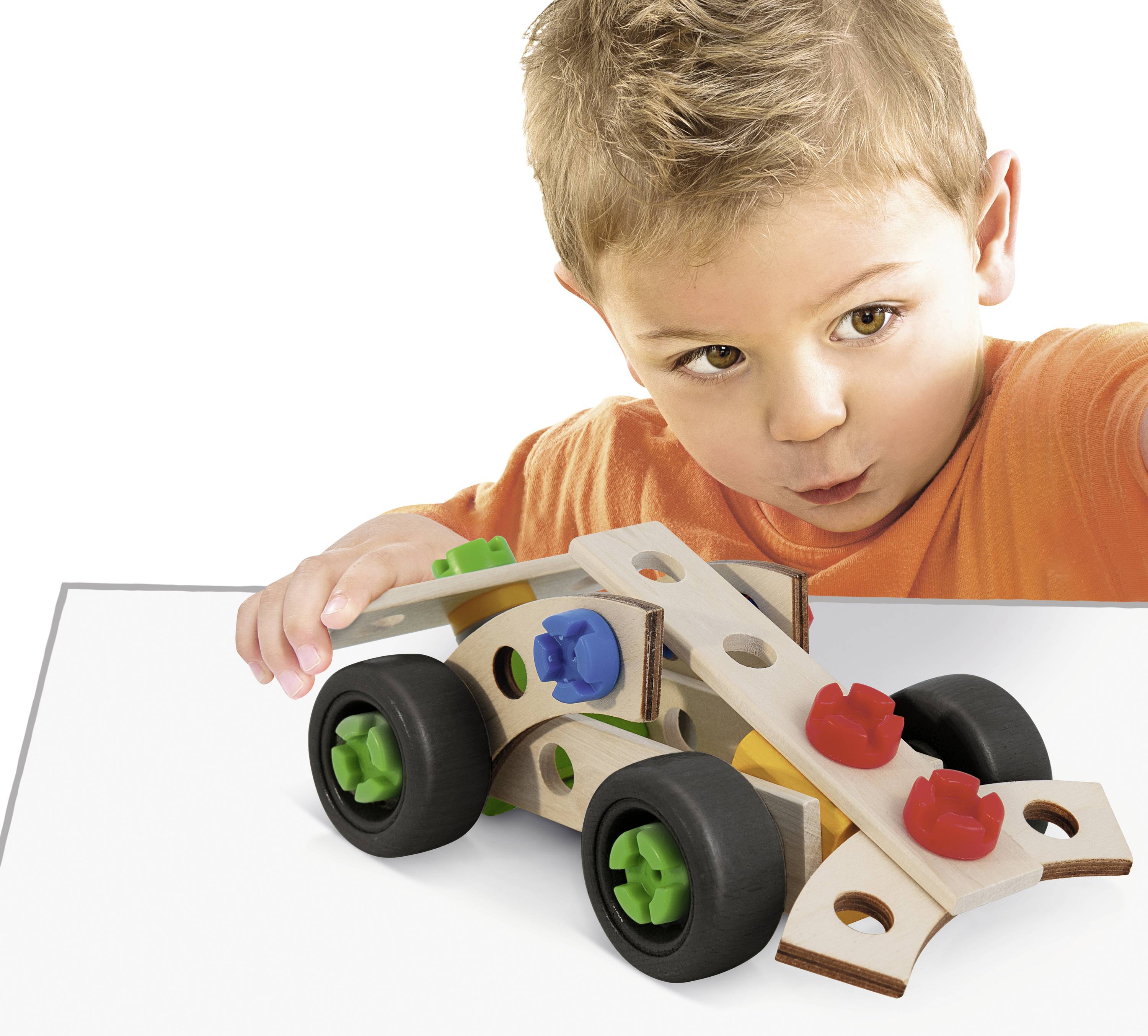 Un enfant portant un t-shirt orange joue avec concentration à une voiture jouet colorée sur une table blanche.