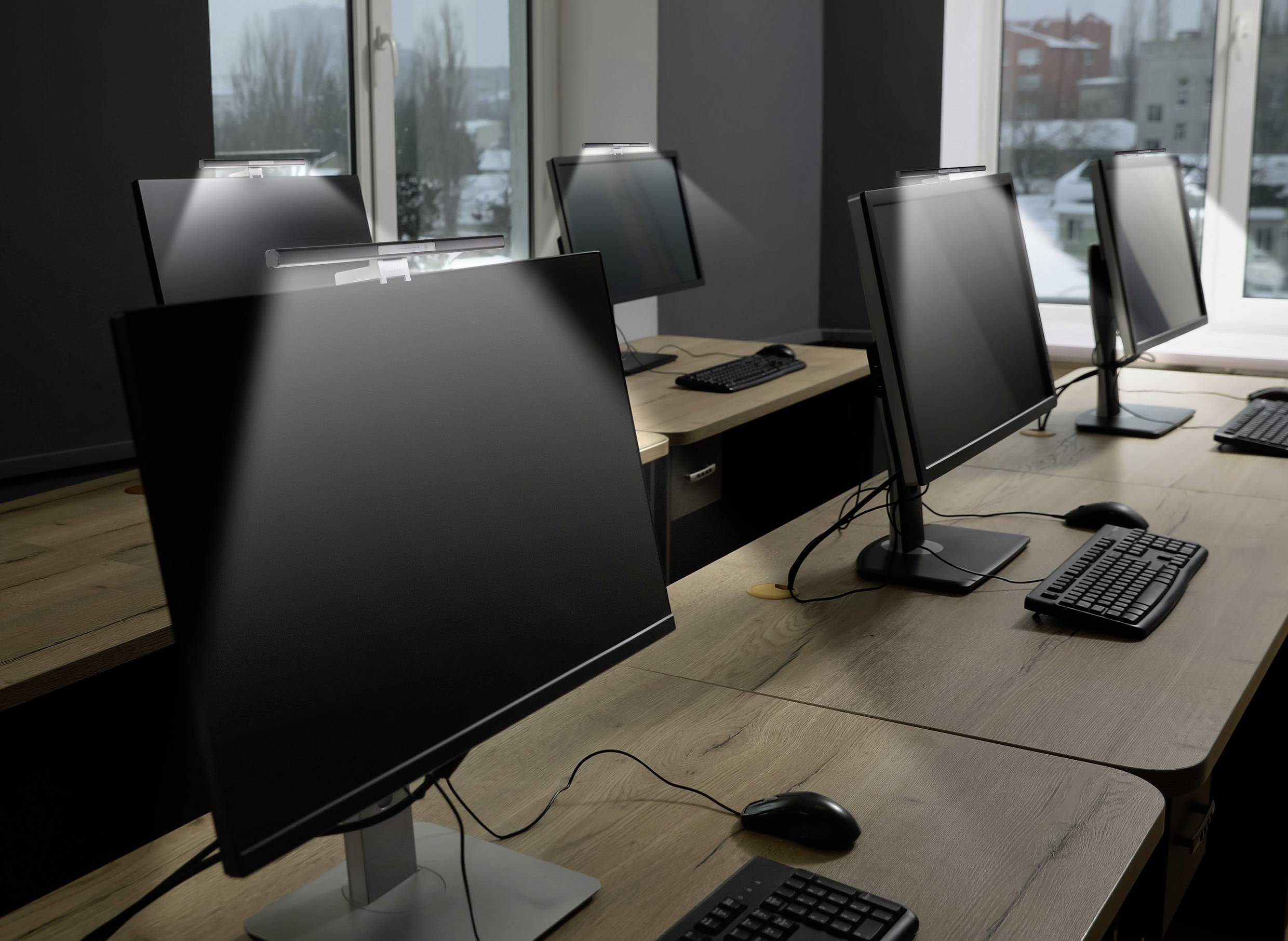 Plusieurs postes de travail informatiques vides dans un bureau moderne, équipés de grands écrans, de claviers et de souris sur des tables en bois.