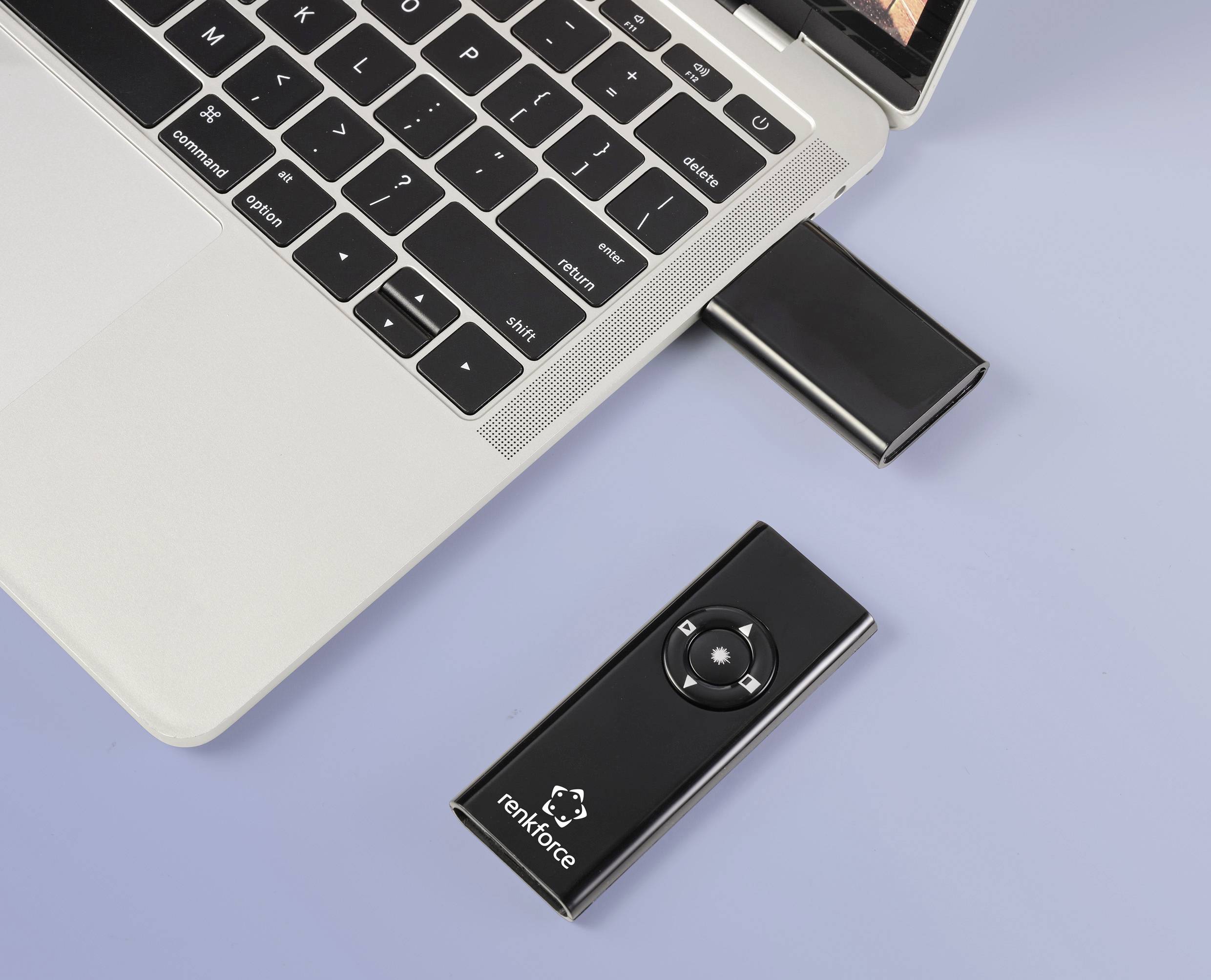 Un ordinateur portable avec une télécommande noire branchée ; à côté se trouve une clé USB. La télécommande possède des touches directionnelles.