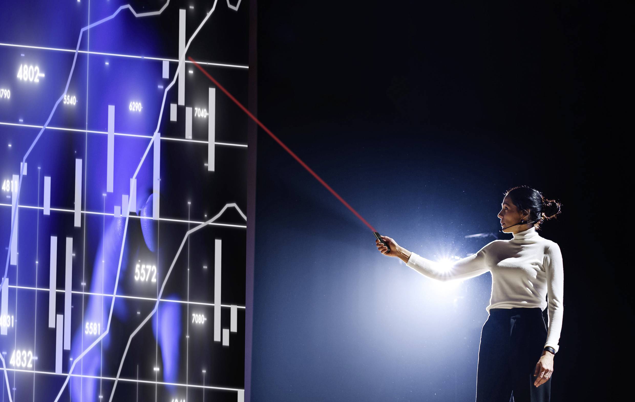 Une femme pointe un diagramme numérique avec des barres et des lignes à l'aide d'un pointeur laser, semblant représenter des données financières.