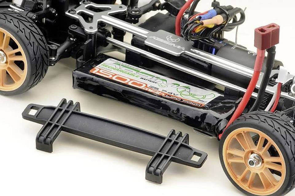 Châssis RC Auto avec batterie et électronique visibles. Roues orange, connexions de câbles et support à côté.