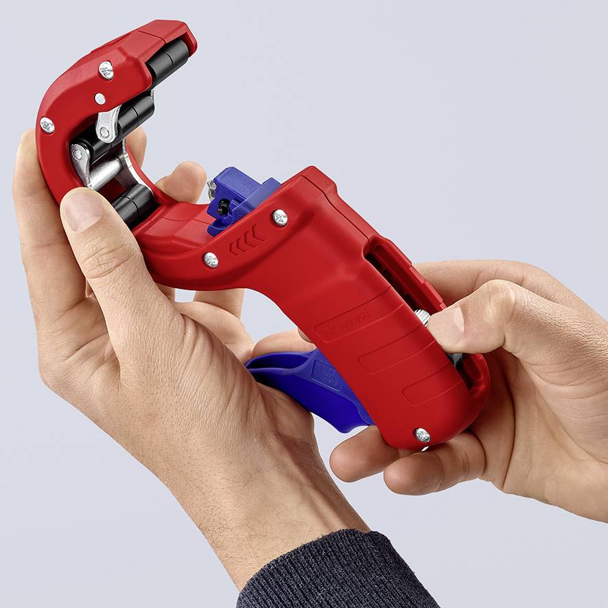 Une main tient un outil rouge utilisé pour couper des tuyaux. Il est stabilisé par la main gauche.