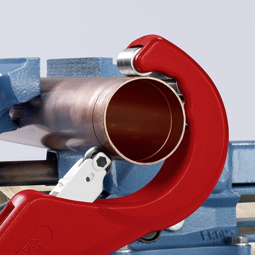 Un tuyau en cuivre est coupé par un coupe-tubes avec une poignée rouge. Le tuyau est posé sur un étau bleu.