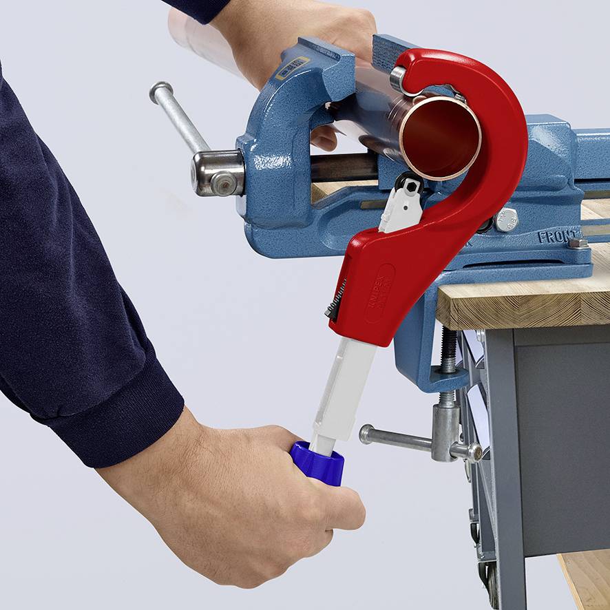 Une personne coupe un tuyau en plastique à l'aide d'un coupe-tube rouge, fixé dans un étau bleu.