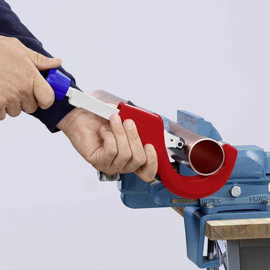 Une personne utilise un coupe-tube pour raccourcir un tuyau de couleur cuivrée, fixé dans un étau de établi.