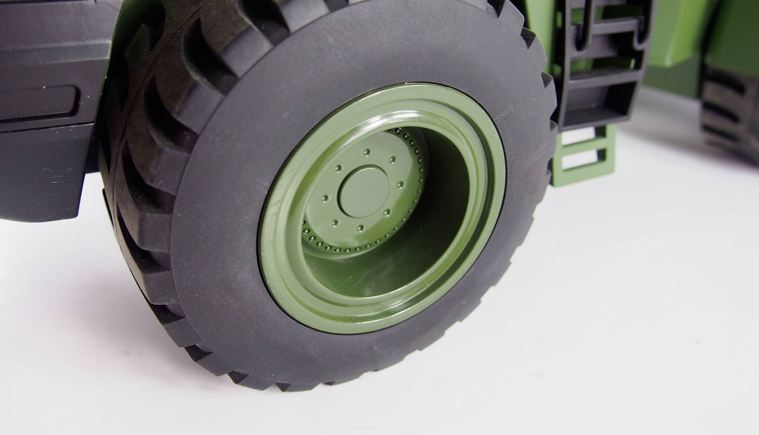 Gros plan d'un pneu de tracteur robuste noir avec une jante verte sur un fond blanc.