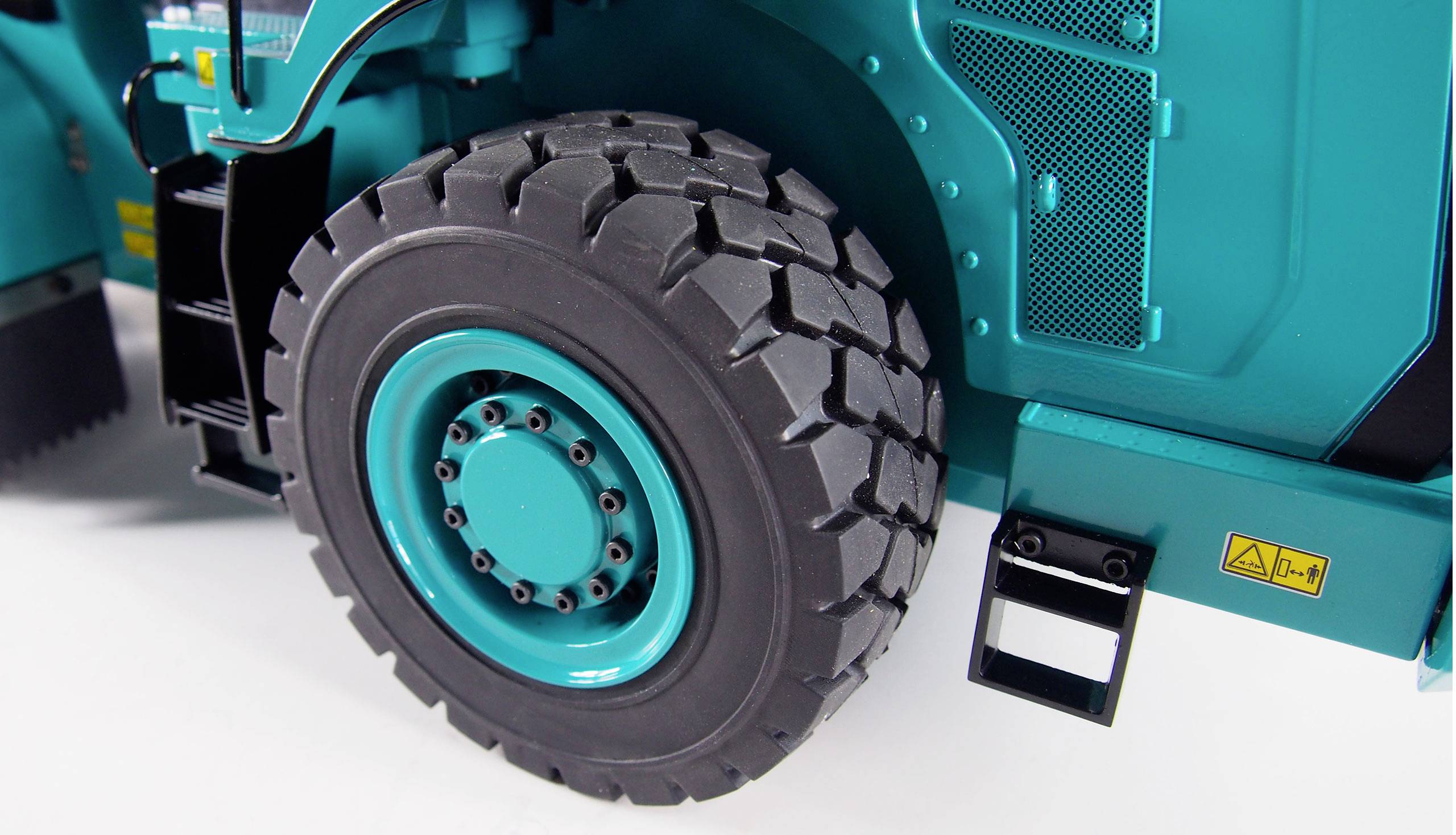 Gros plan d'un pneu gris foncé sur un véhicule turquoise, probablement un engin industriel. Certains détails sont visibles.