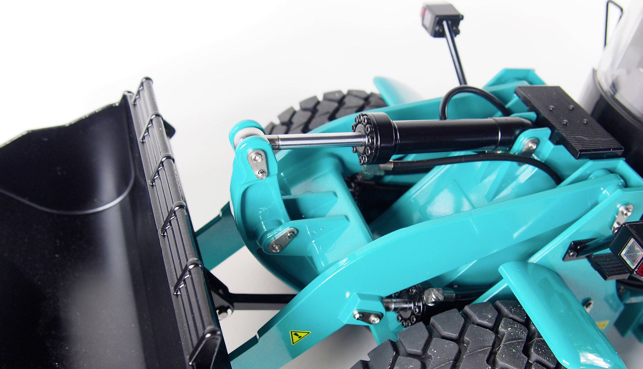 Gros plan d'un chargeur à roues bleu clair, photographié sur un fond blanc. On peut voir la pelle, le système hydraulique et les pneus.