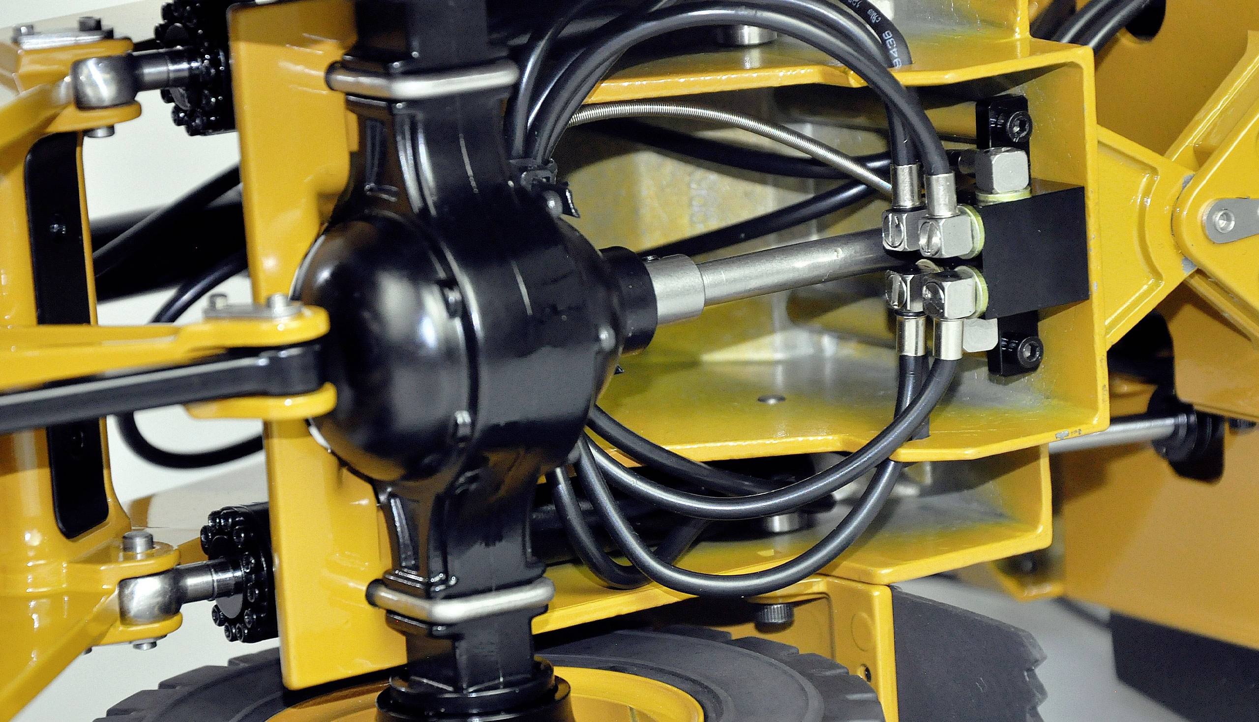 Gros plan d'un appareil mécanique jaune avec des conduites hydrauliques noires et des connexions métalliques. Des détails de tuyaux et de vis sont visibles.