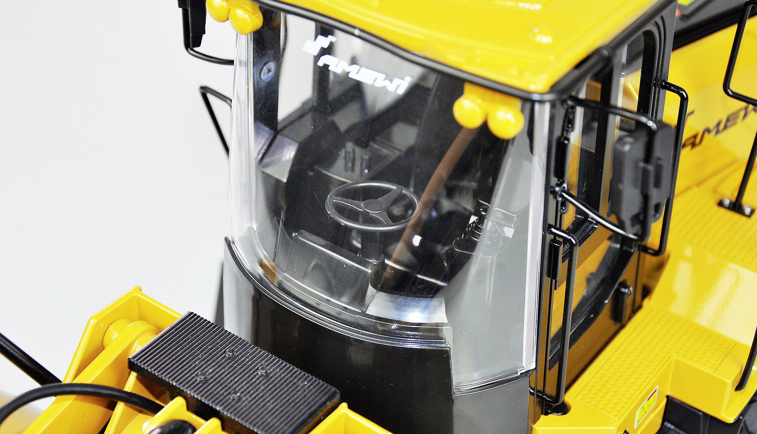 'Gros plan d'une cabine de véhicule de construction jaune avec un volant noir et des vitres transparentes, sans conducteur visible.'