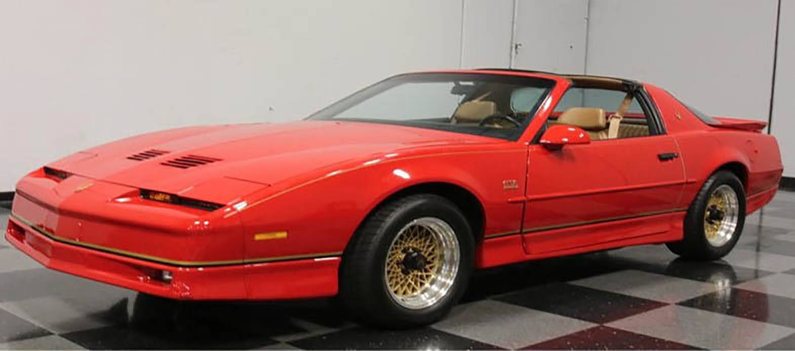 Coupé de sport rouge dans un style rétro, montrant une forme de carrosserie prononcée et des jantes dorées, garé dans un espace d'exposition.