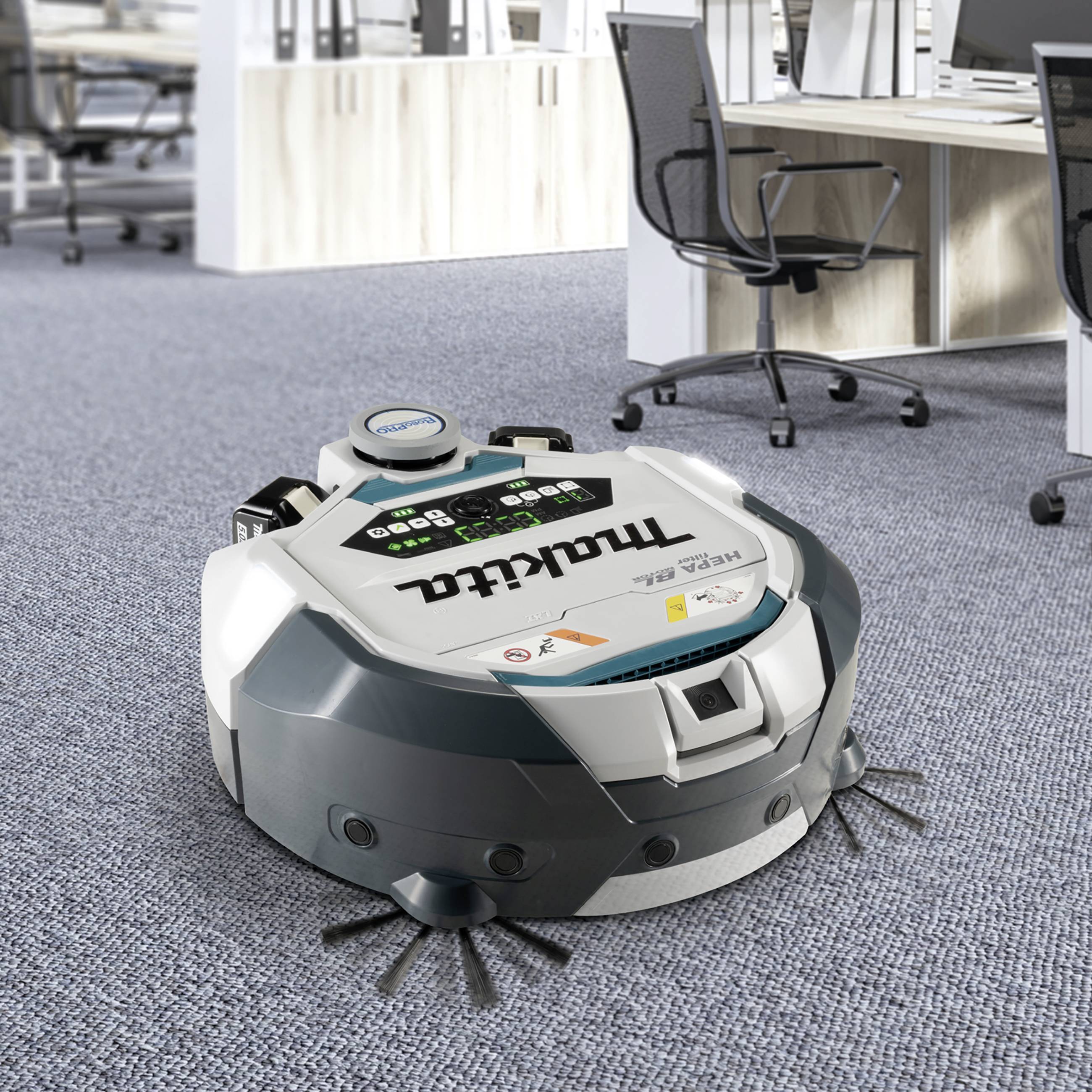 Un robot aspirateur nettoie le tapis dans un bureau moderne avec des bureaux et des chaises en arrière-plan.