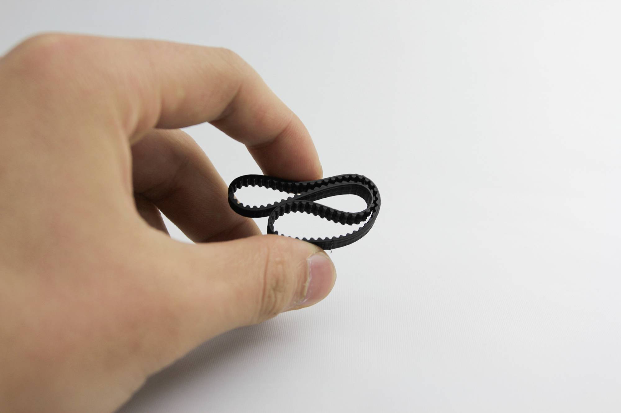 Une main tient un petit élastique noir devant un fond neutre.