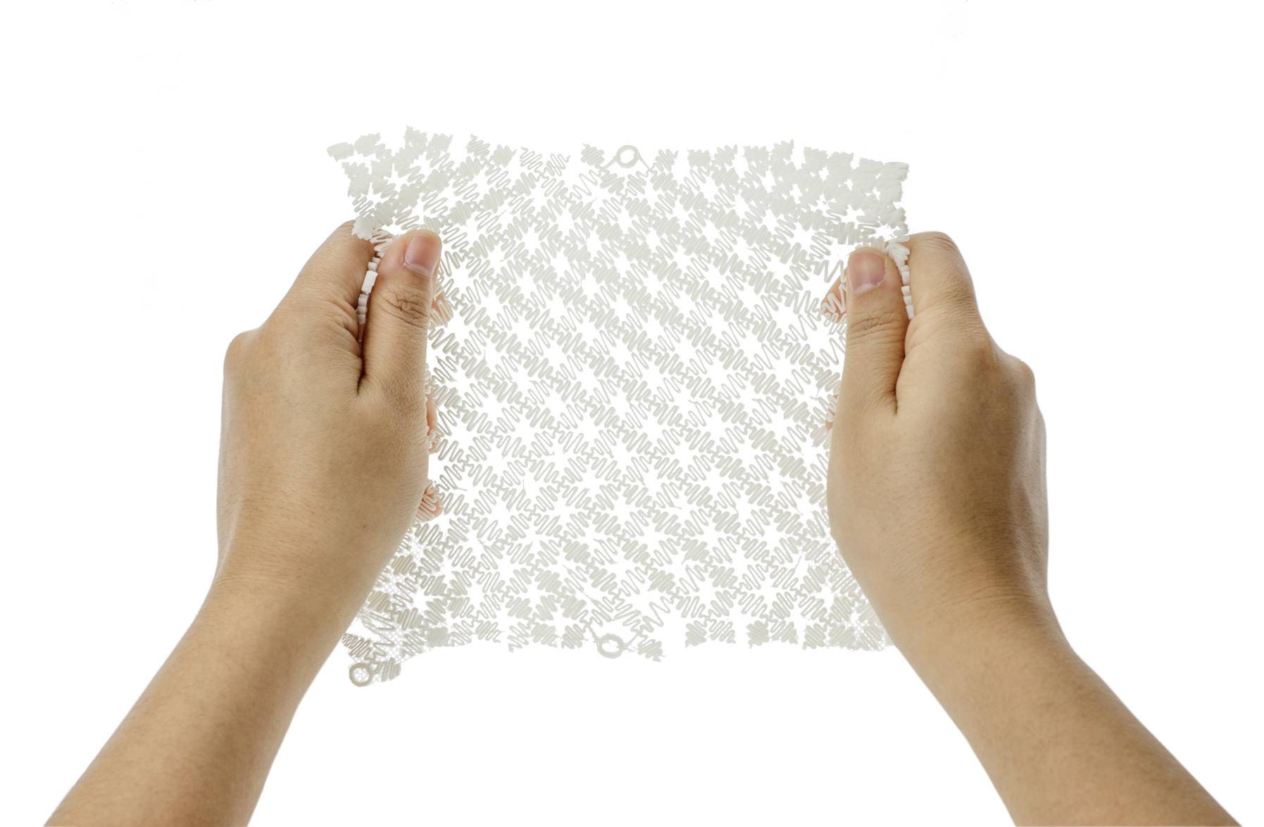 Deux mains tiennent un matériau flexible et transparent présentant un motif en losange sur un fond blanc.