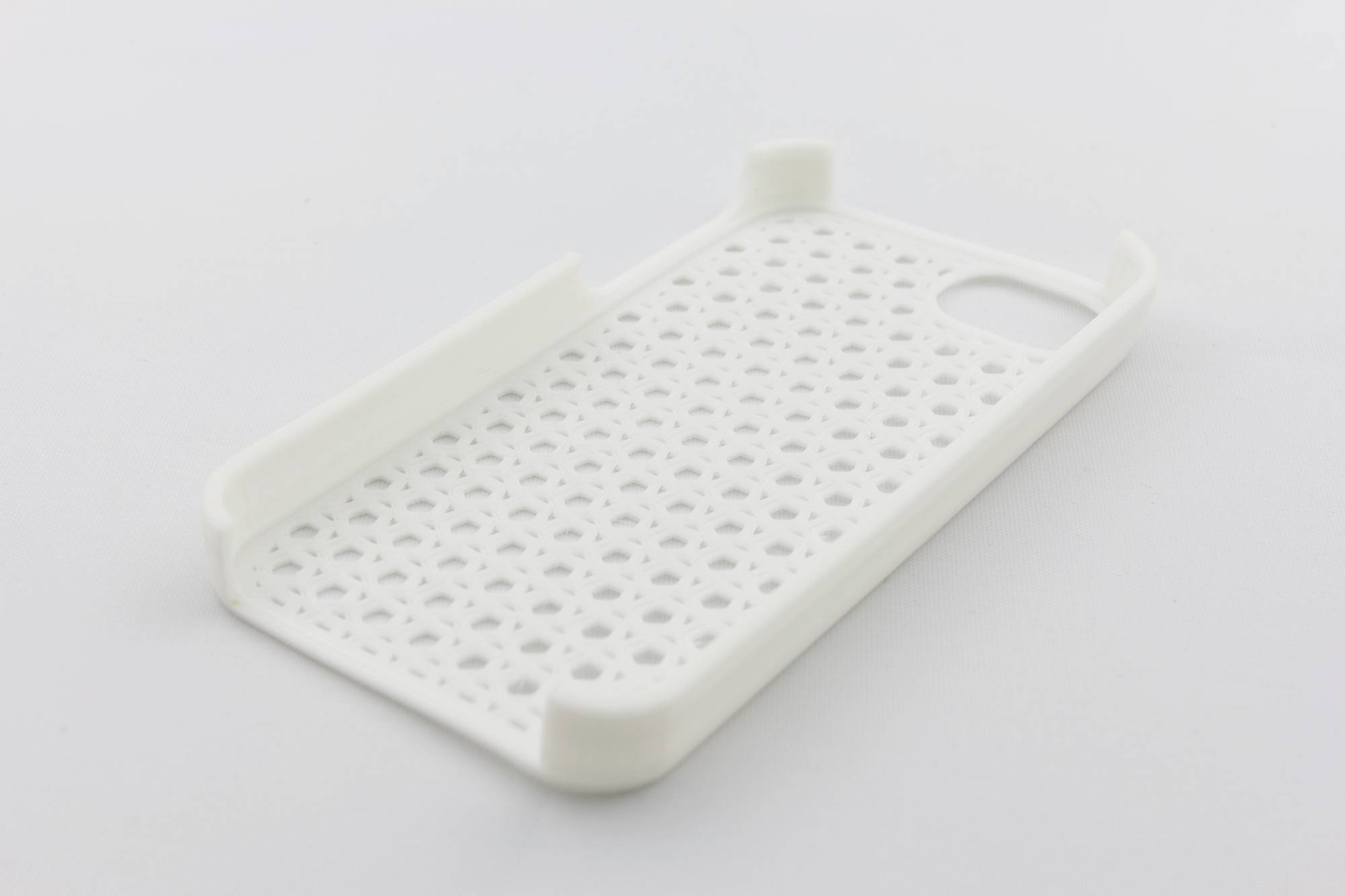 Étui de téléphone blanc en plastique perforé, posé à plat sur un fond gris, face arrière vers le haut.