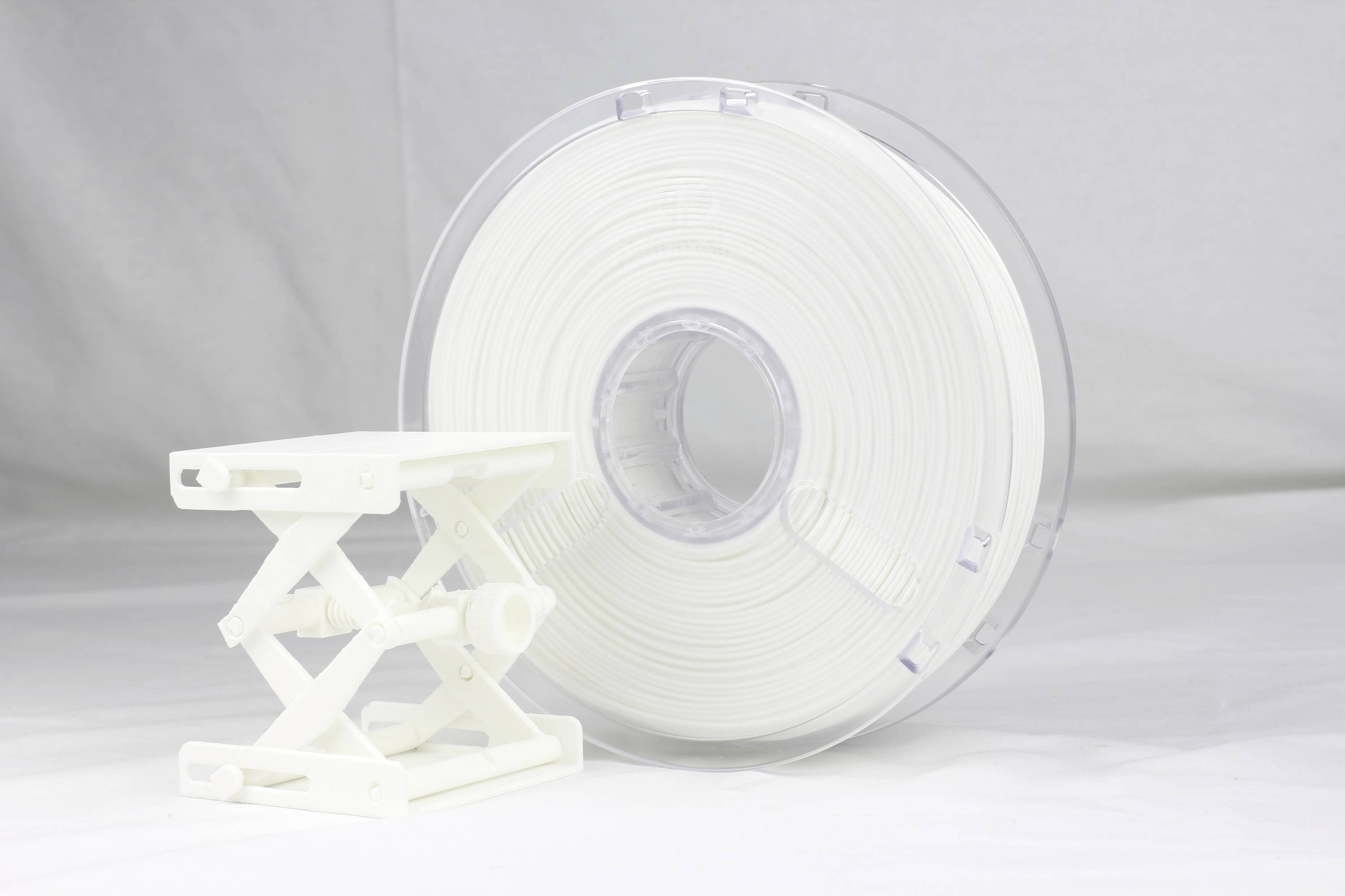 Une bobine de filament d'imprimante 3D blanche et une petite table blanche réglable en hauteur sont posées sur un fond gris clair.
