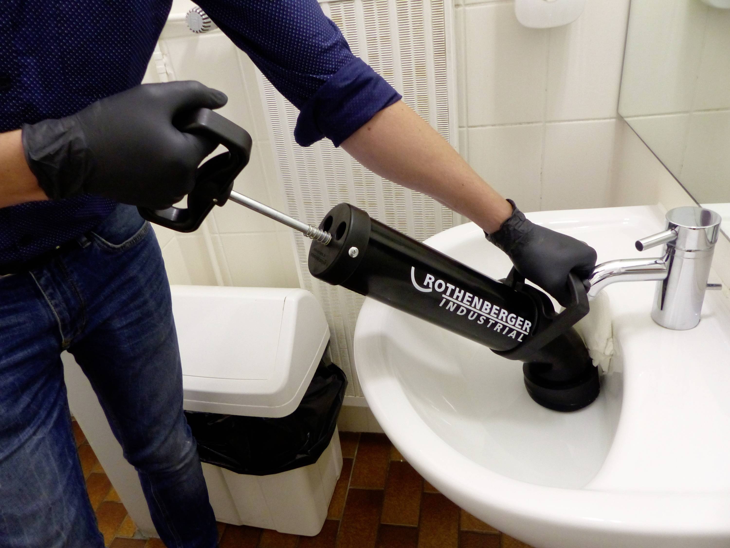 Une personne portant des gants utilise une pompe de débouchage pour désengorger un lavabo.