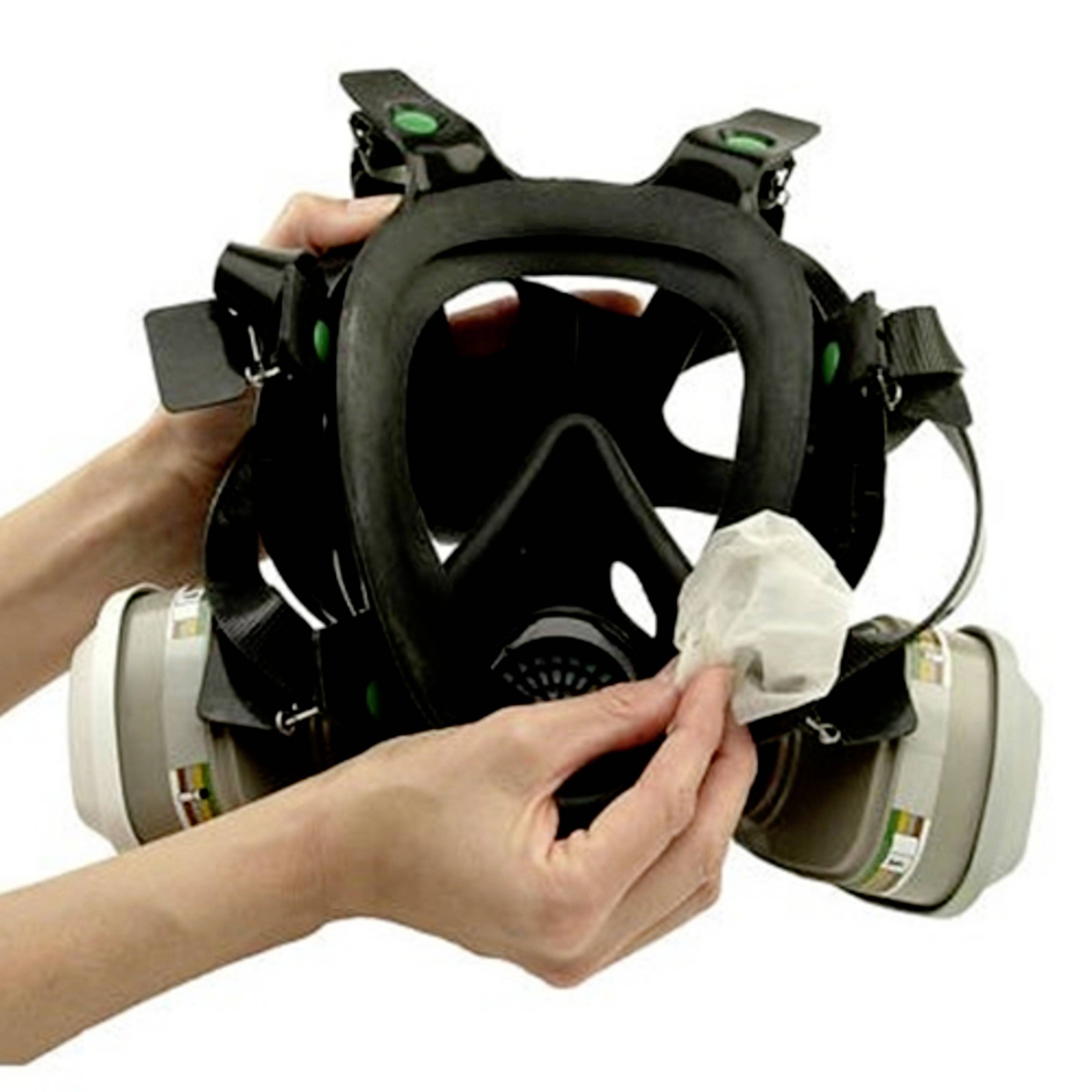 Une main tient un masque de protection destiné à un usage industriel. Une deuxième main essuie l'intérieur du masque avec un chiffon.