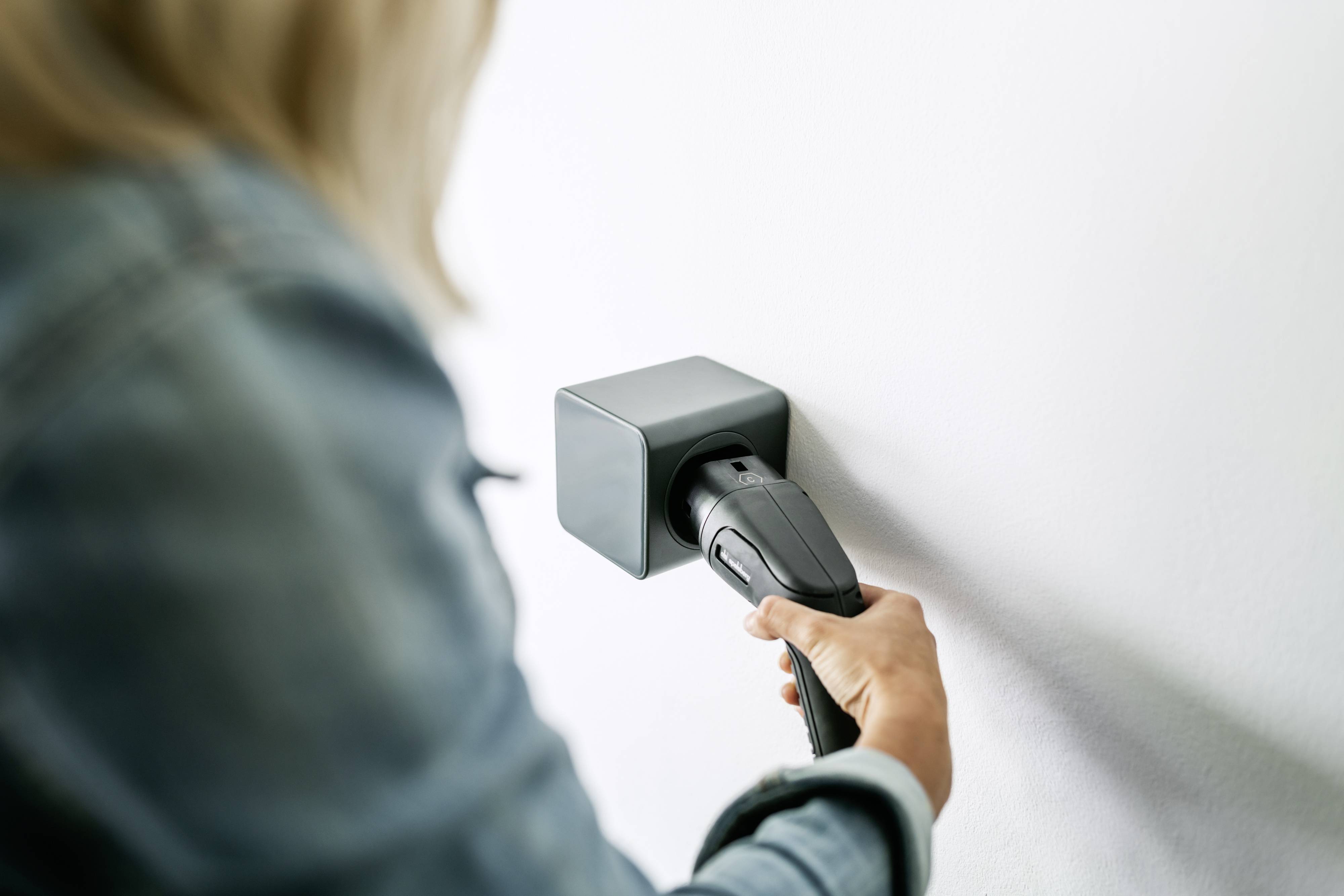 Une personne branche un câble de charge dans une prise murale. Concentré sur le processus de charge, probablement pour un appareil électronique.