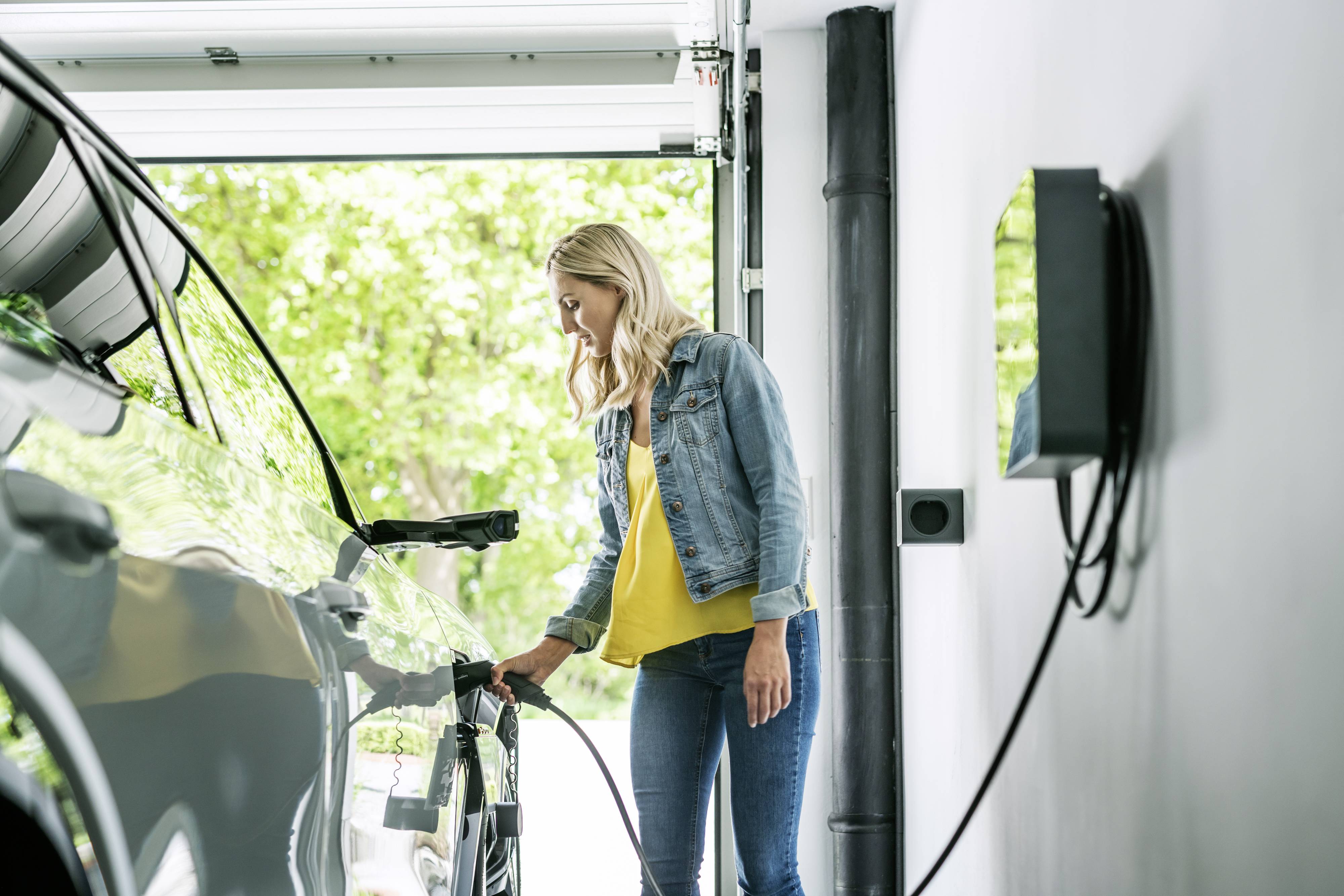 Une personne charge un véhicule électrique dans un garage en branchant un câble de recharge au véhicule.