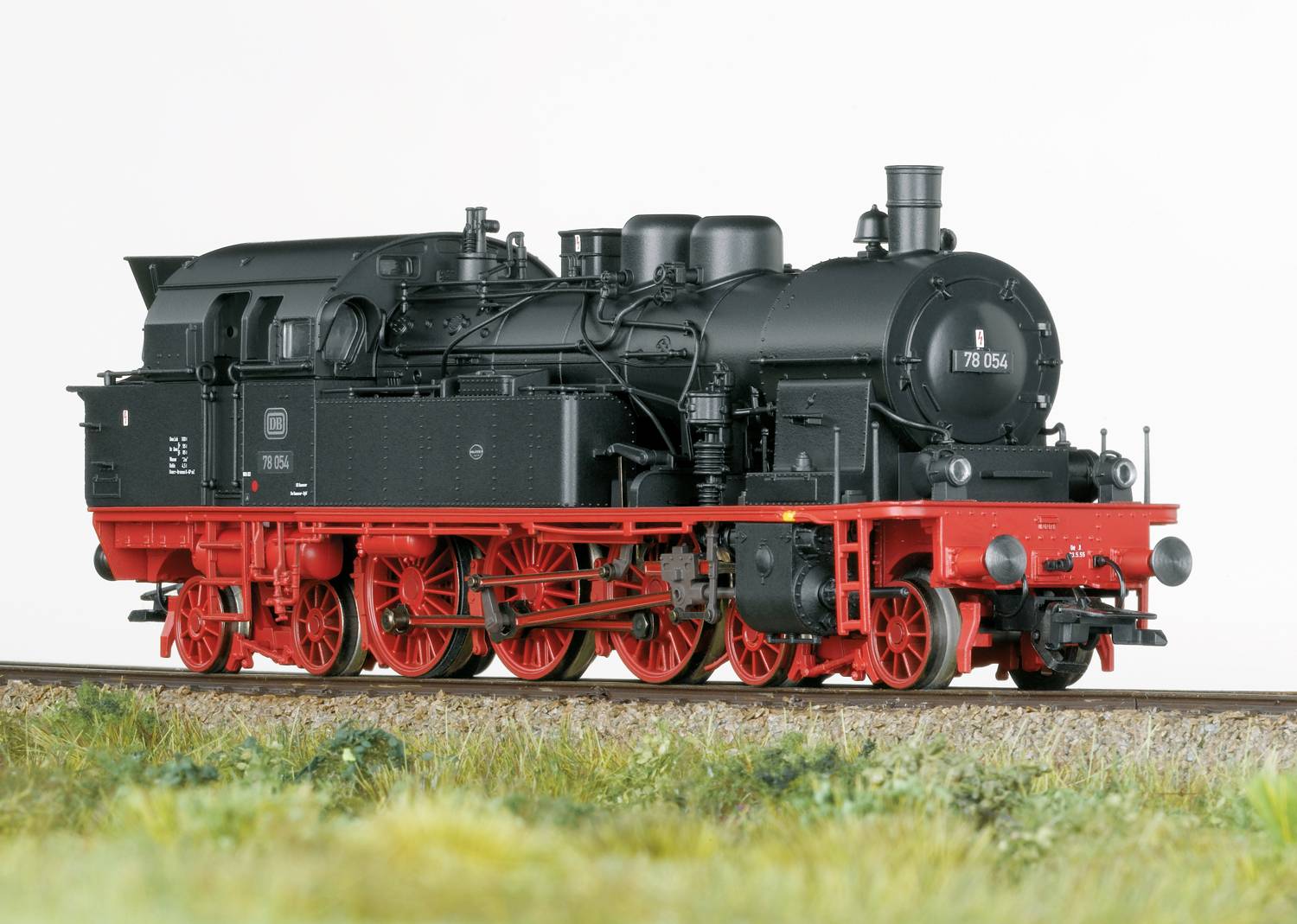Une locomotive à vapeur noire avec des roues rouges est immobilisée sur des rails. Elle possède une chaudière ronde et de nombreux détails techniques.