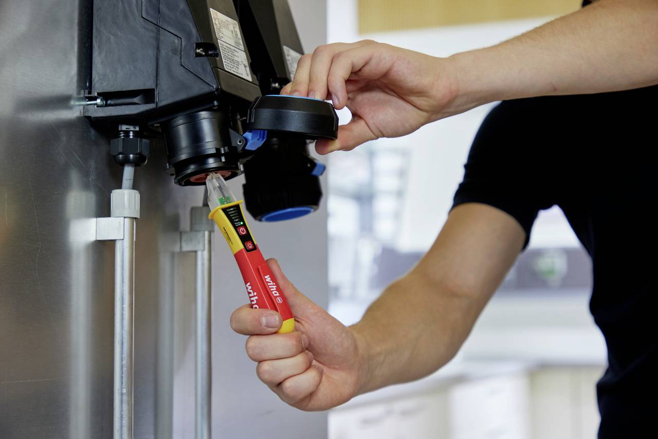 Une personne utilise un dispositif de test pour mesurer la tension sur une installation électrique dans un environnement industriel.