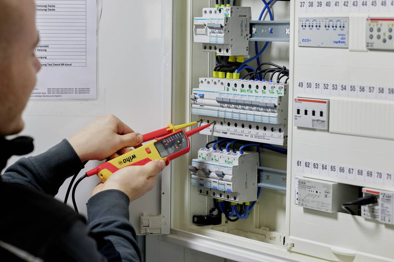 Une personne vérifie le câblage dans un armoire électrique à l'aide d'un testeur de tension. L'accent est mis sur la sécurité et la fonctionnalité.