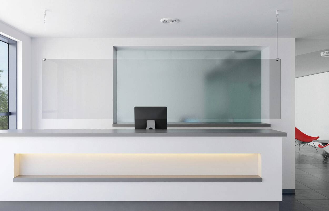 Espace d'accueil moderne avec un bureau, un écran d'ordinateur et une séparation en plexiglas ; architecture rectangulaire.