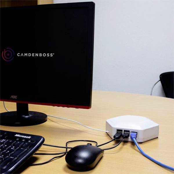 Ein Computerbildschirm und eine Tastatur sind mit einem kleinen weißen Router verbunden, der auf einem Tisch steht.