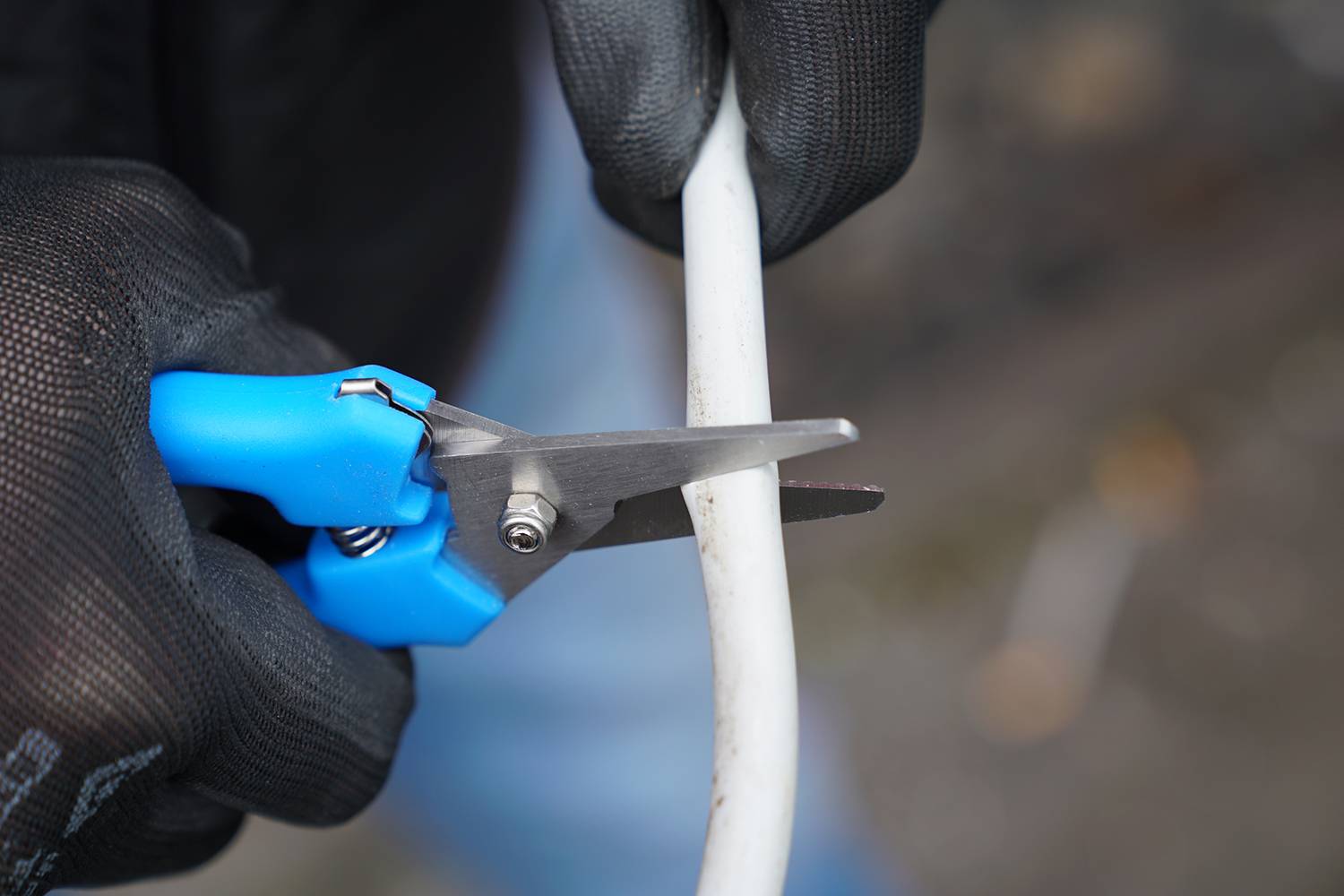 Une personne portant des gants noirs coupe un câble blanc avec des ciseaux bleus.