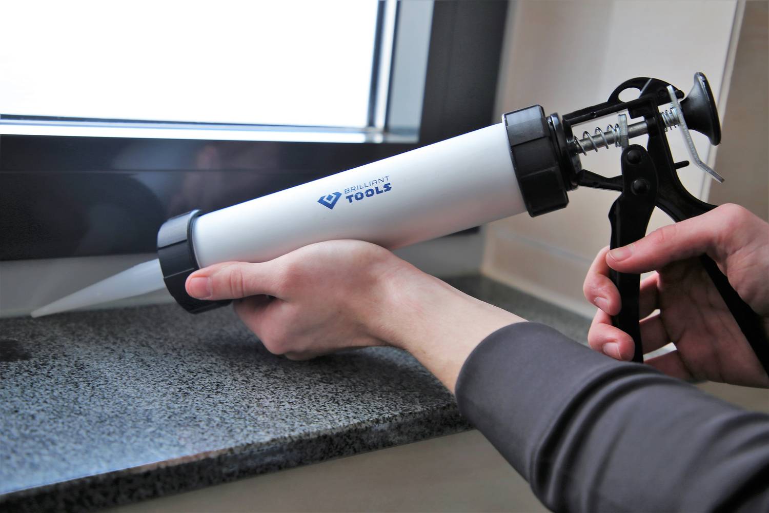 Une personne utilise un pistolet à cartouche pour appliquer un mastic d'étanchéité sur la jointure d'un châssis de fenêtre afin d'assurer l'isolation et la protection.