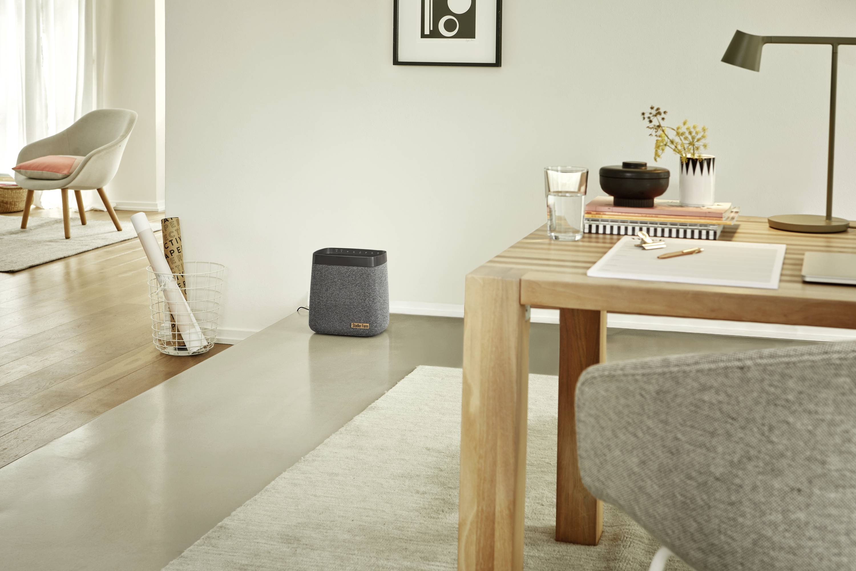 Un salon moderne avec une table sur laquelle sont posés des livres et une lampe de bureau. À l'arrière-plan, un fauteuil et un haut-parleur.