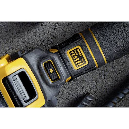 Gros plan sur une poignée d'outil électrique noir et jaune sur une surface en béton gris, montrant un indicateur de réglage de puissance et un bouton de commande.