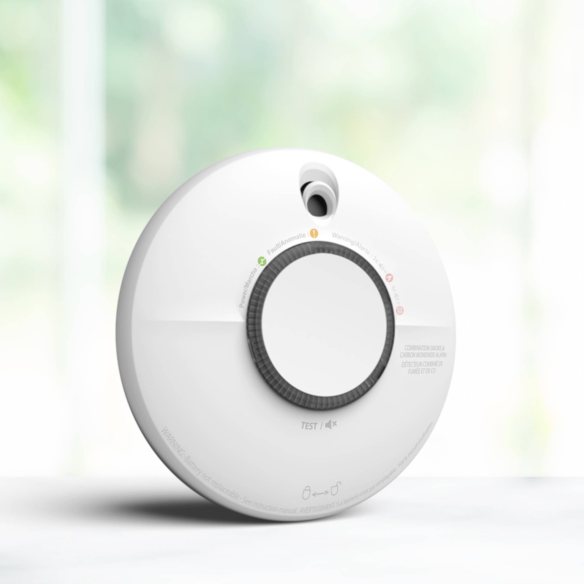 Un détecteur de fumée en gros plan avec un grand bouton central et des voyants lumineux d'état. L'arrière-plan est flou.